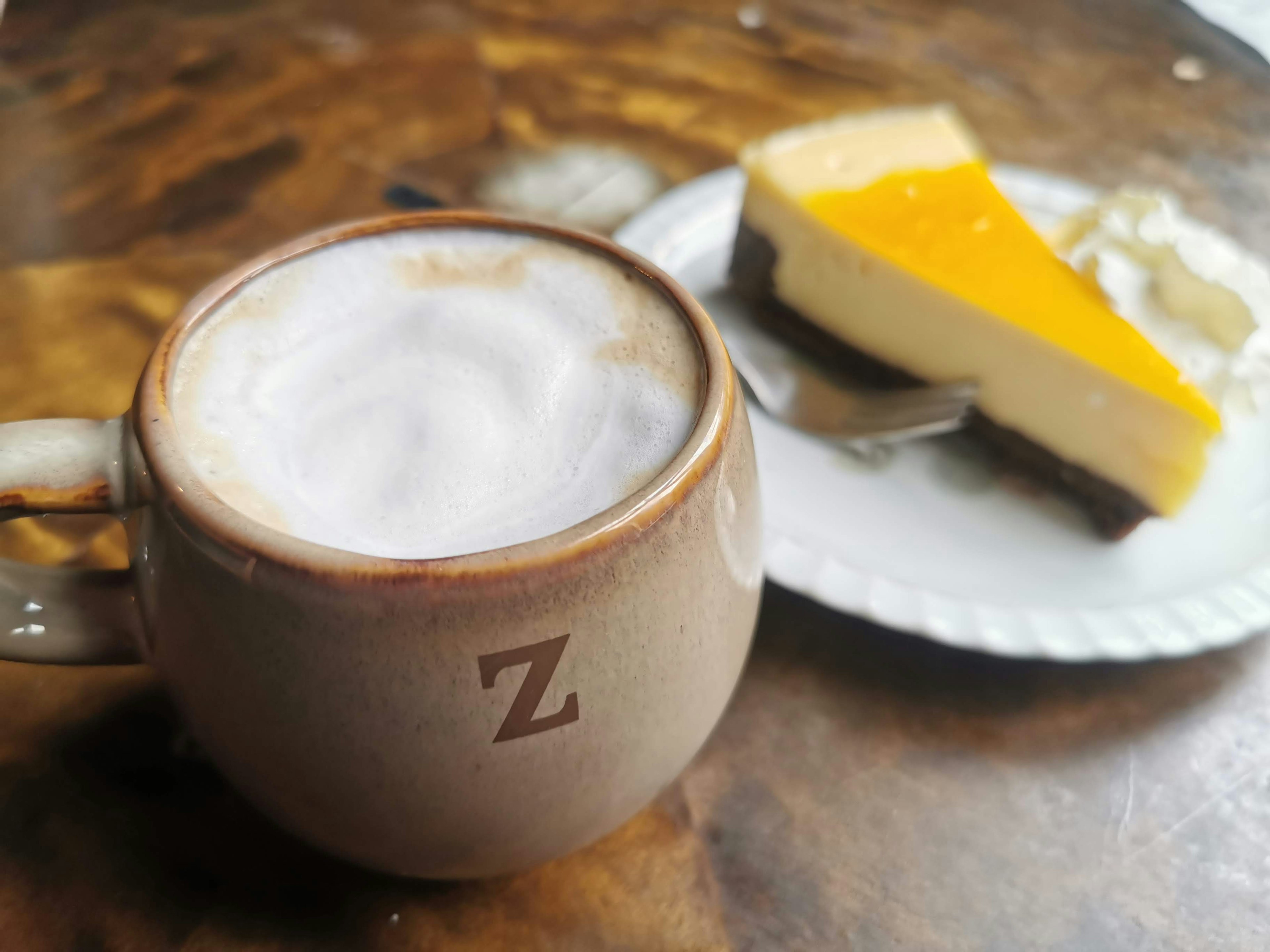 Una taza de café con espuma al lado de una rebanada de cheesecake de naranja