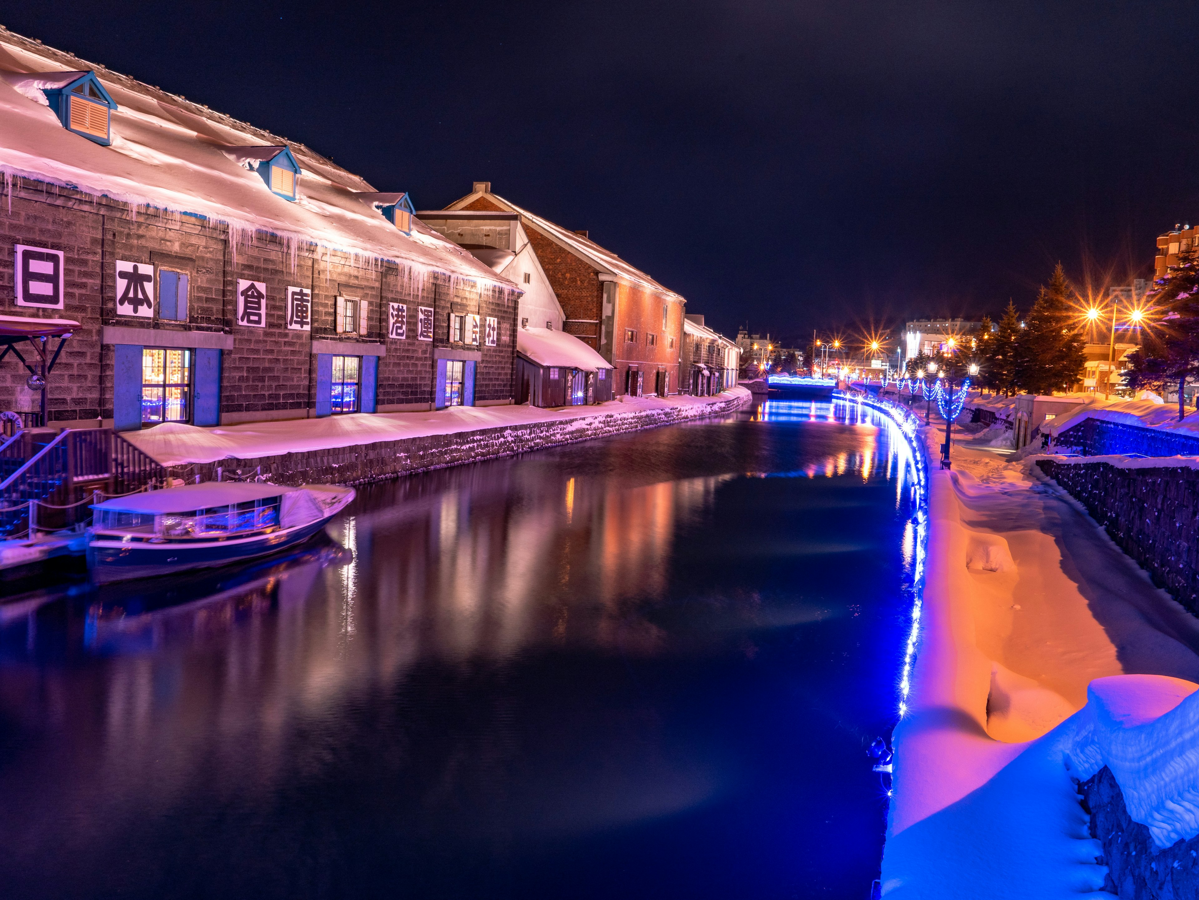 Schneebedeckter Kanal bei Nacht mit leuchtenden blauen Lichtern und Gebäuden