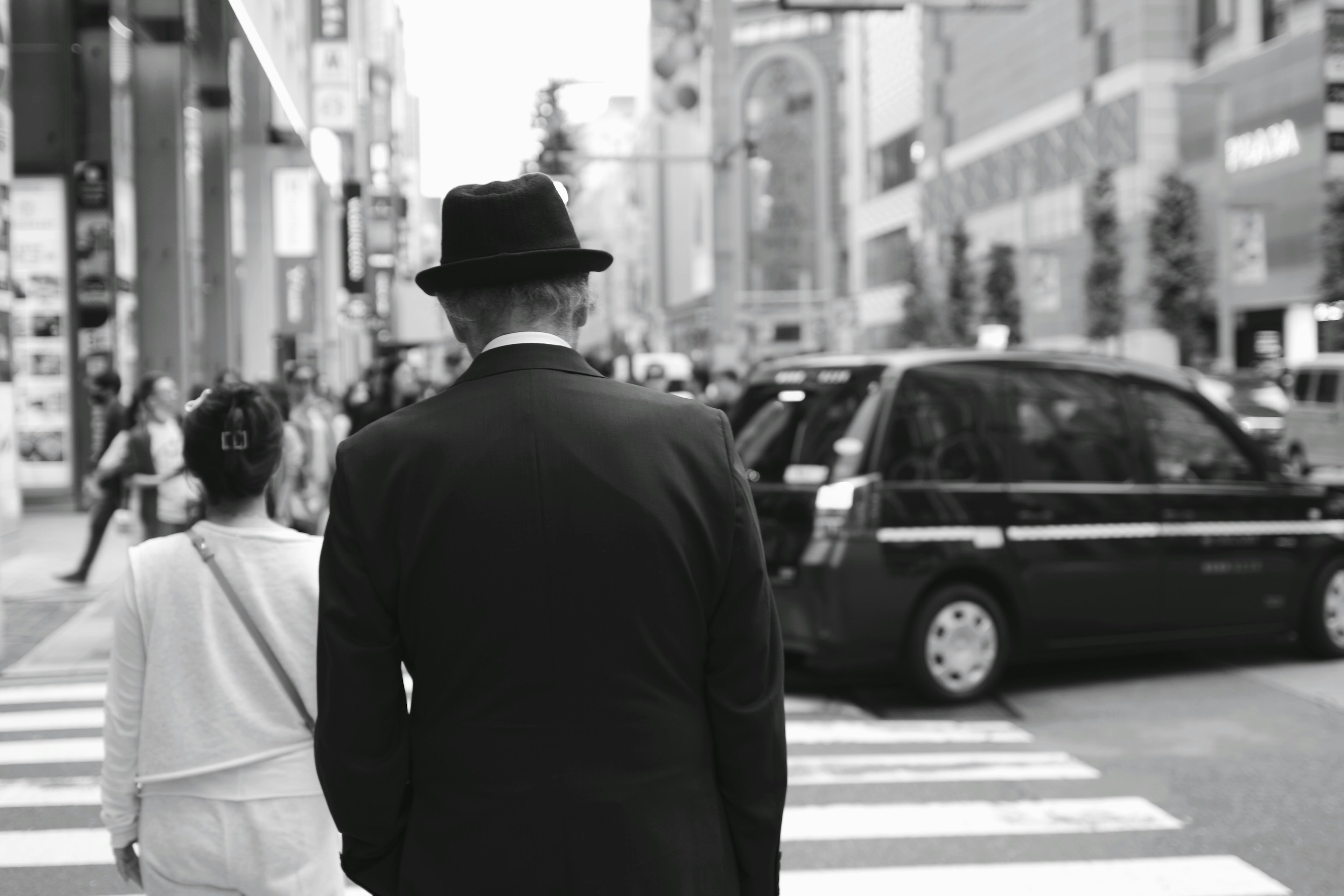 黒いスーツと帽子を着た男性が女性と一緒に横断歩道を渡るモノクロ写真