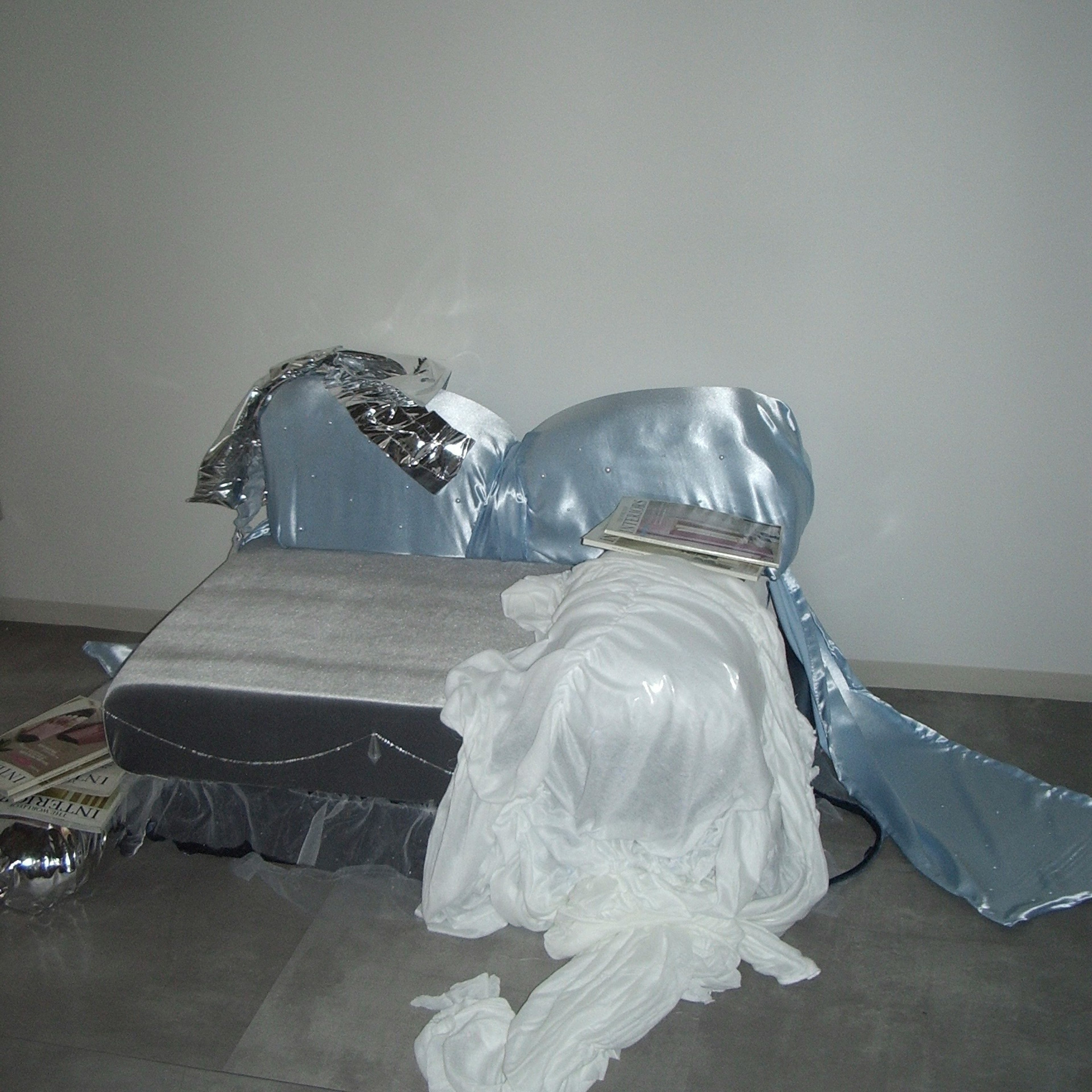 A corner of a room featuring a sofa covered with silver and white fabrics along with magazines