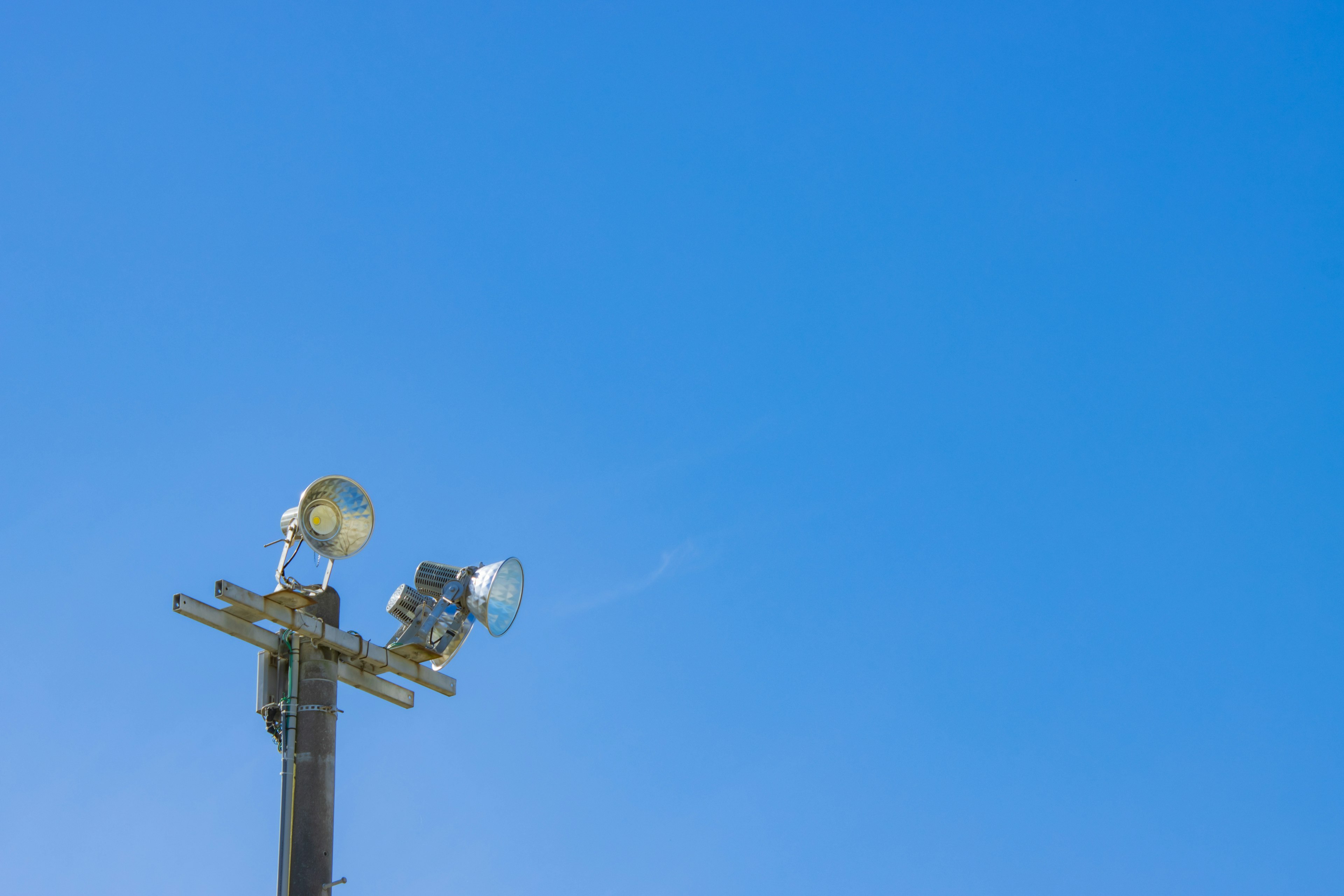 Strommast mit zwei Flutlichtscheinwerfern vor klarem blauen Himmel