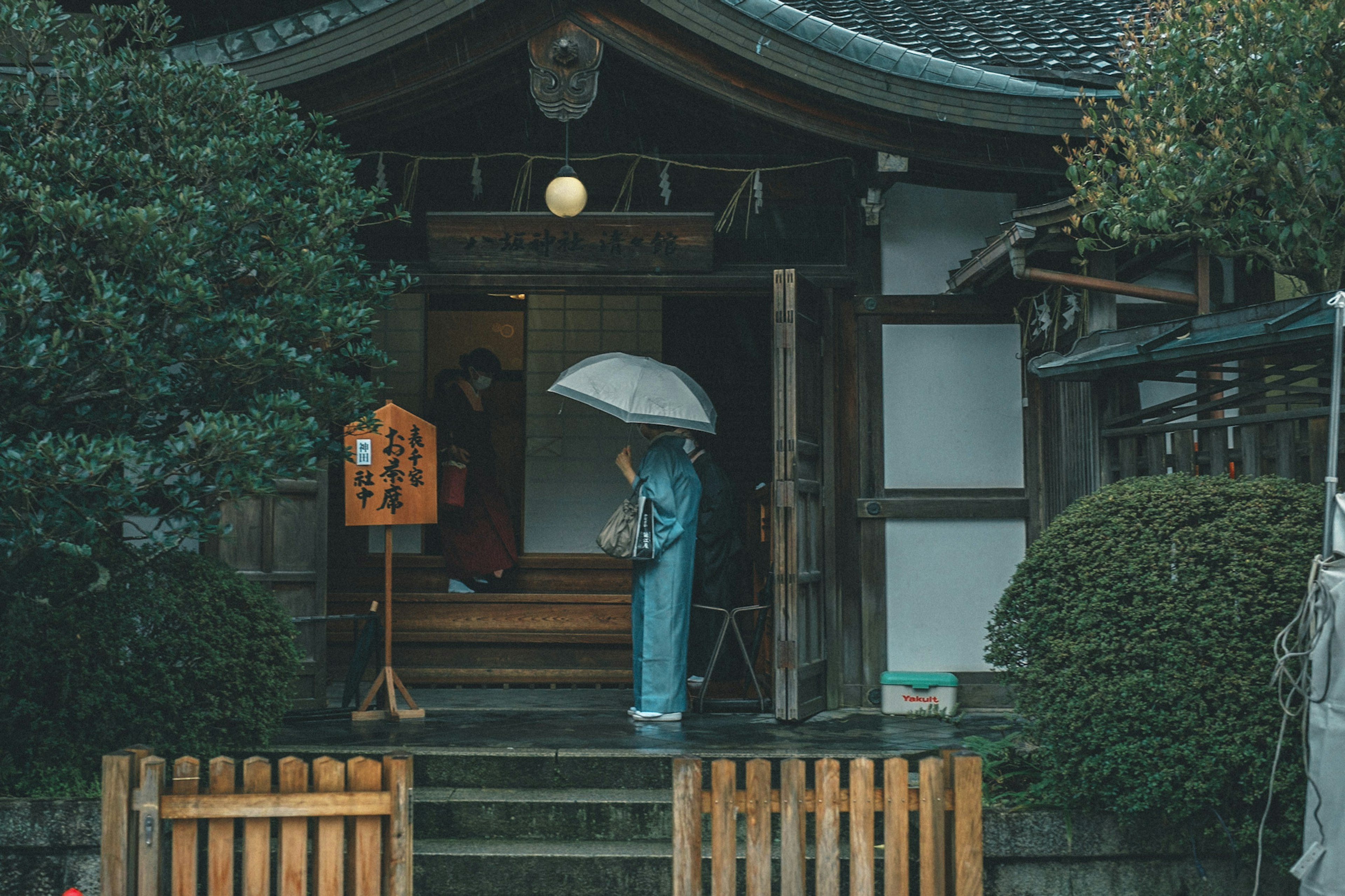 A person in a blue kimono holding an umbrella standing in front of a traditional Japanese building