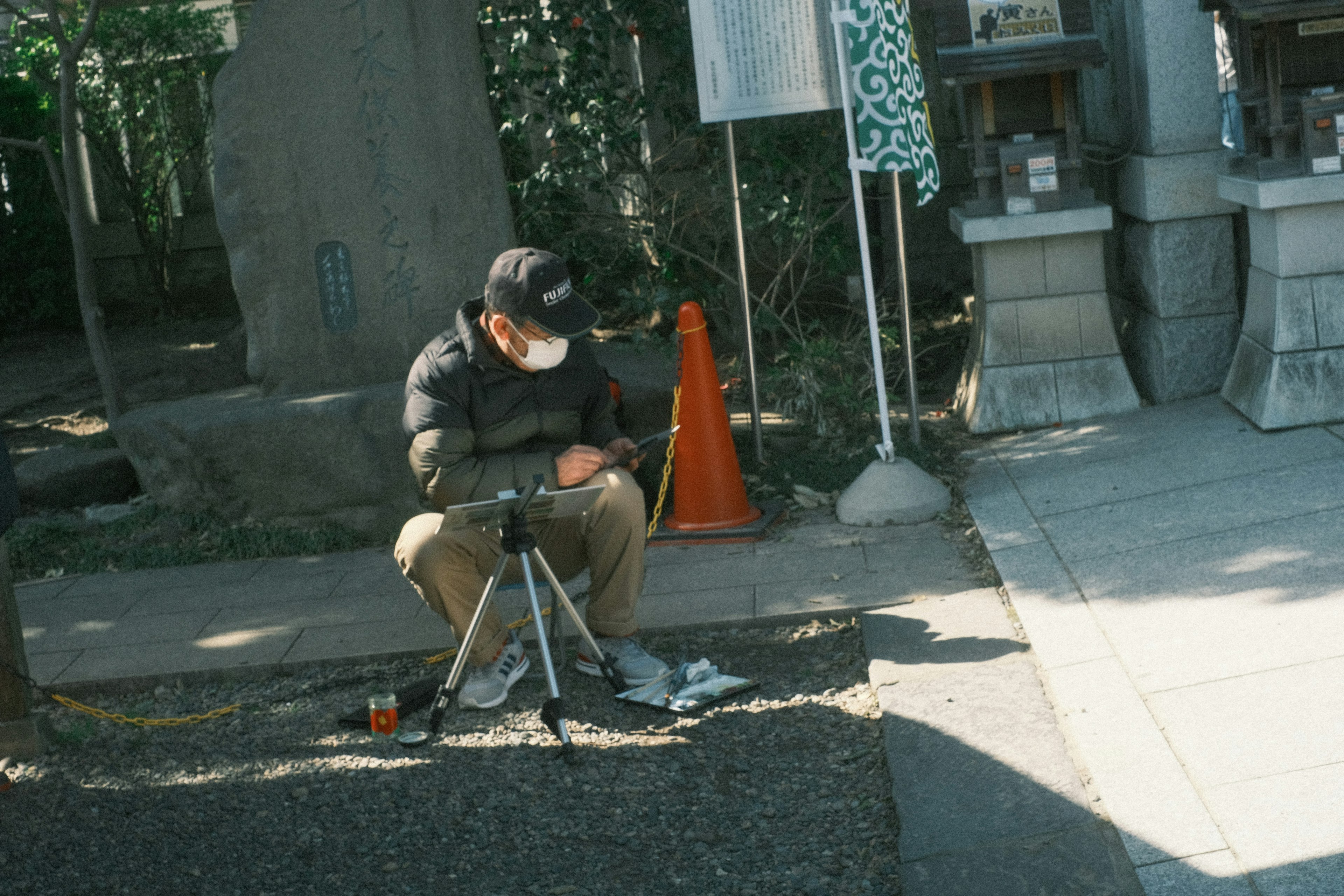 公園で三脚を使っている男性の写真　オレンジのコーンと周囲の緑が特徴