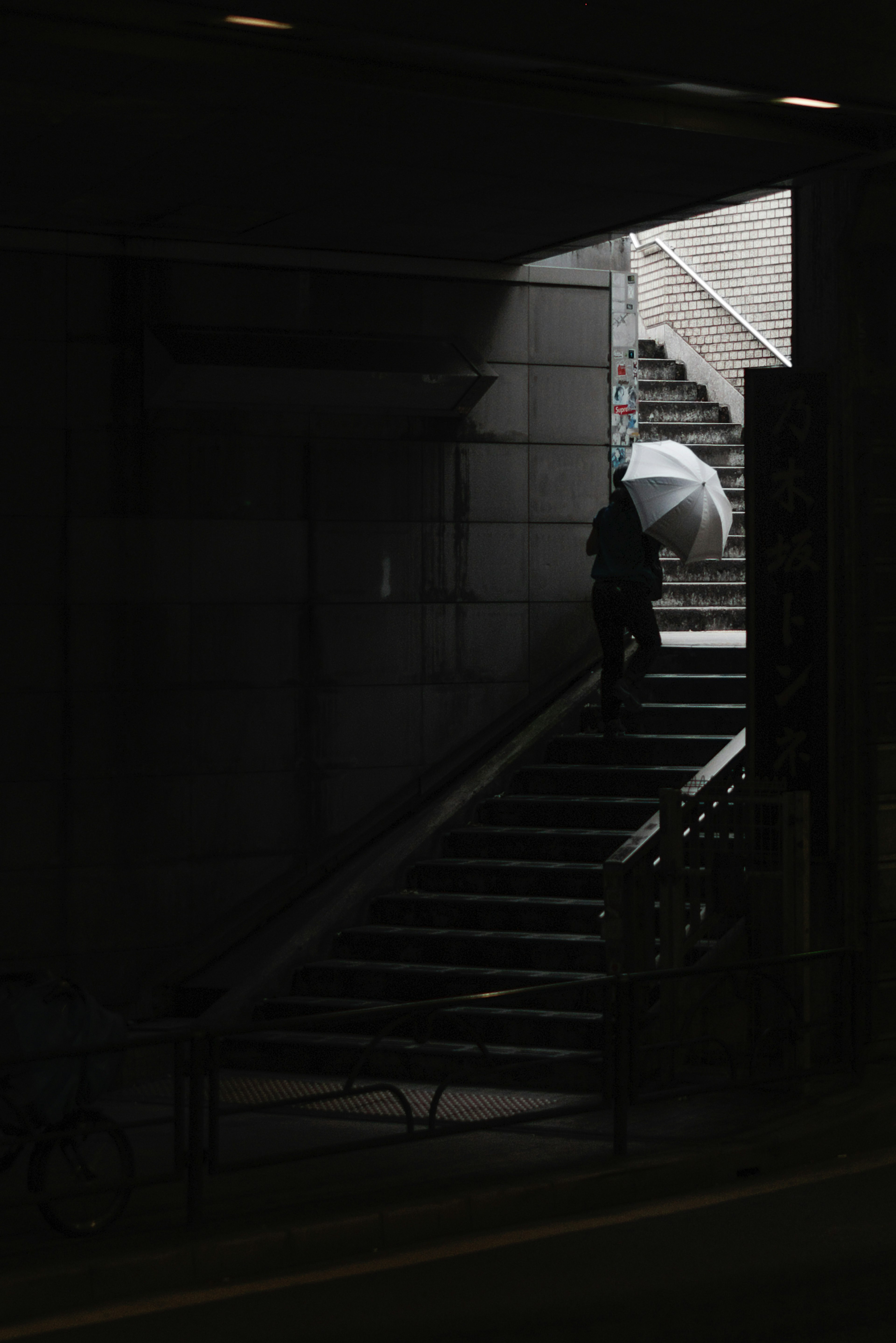 Silhouette of a person with an umbrella ascending stairs in a dark passage