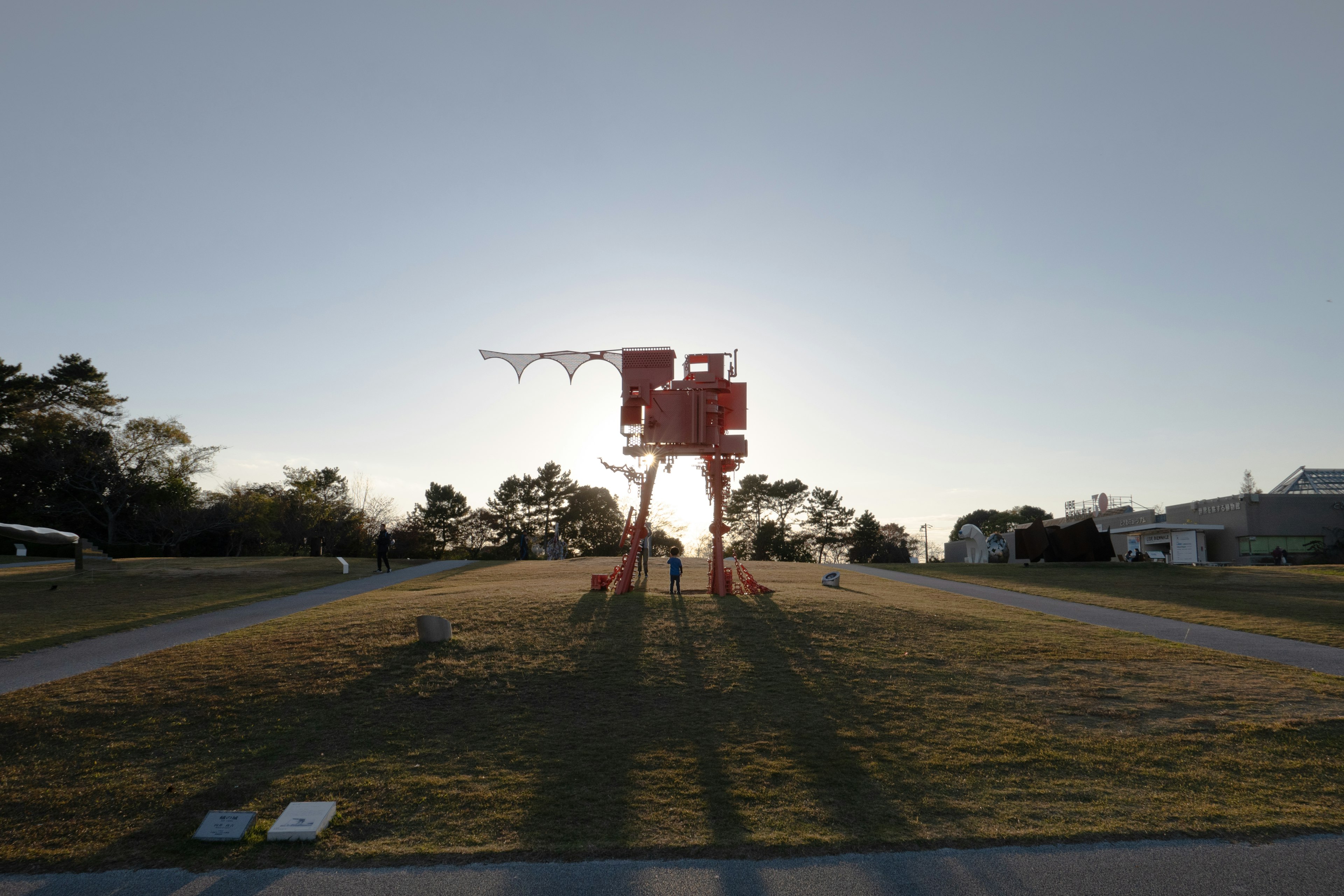 Una scultura rossa si erge in un parco con il sole al tramonto sullo sfondo