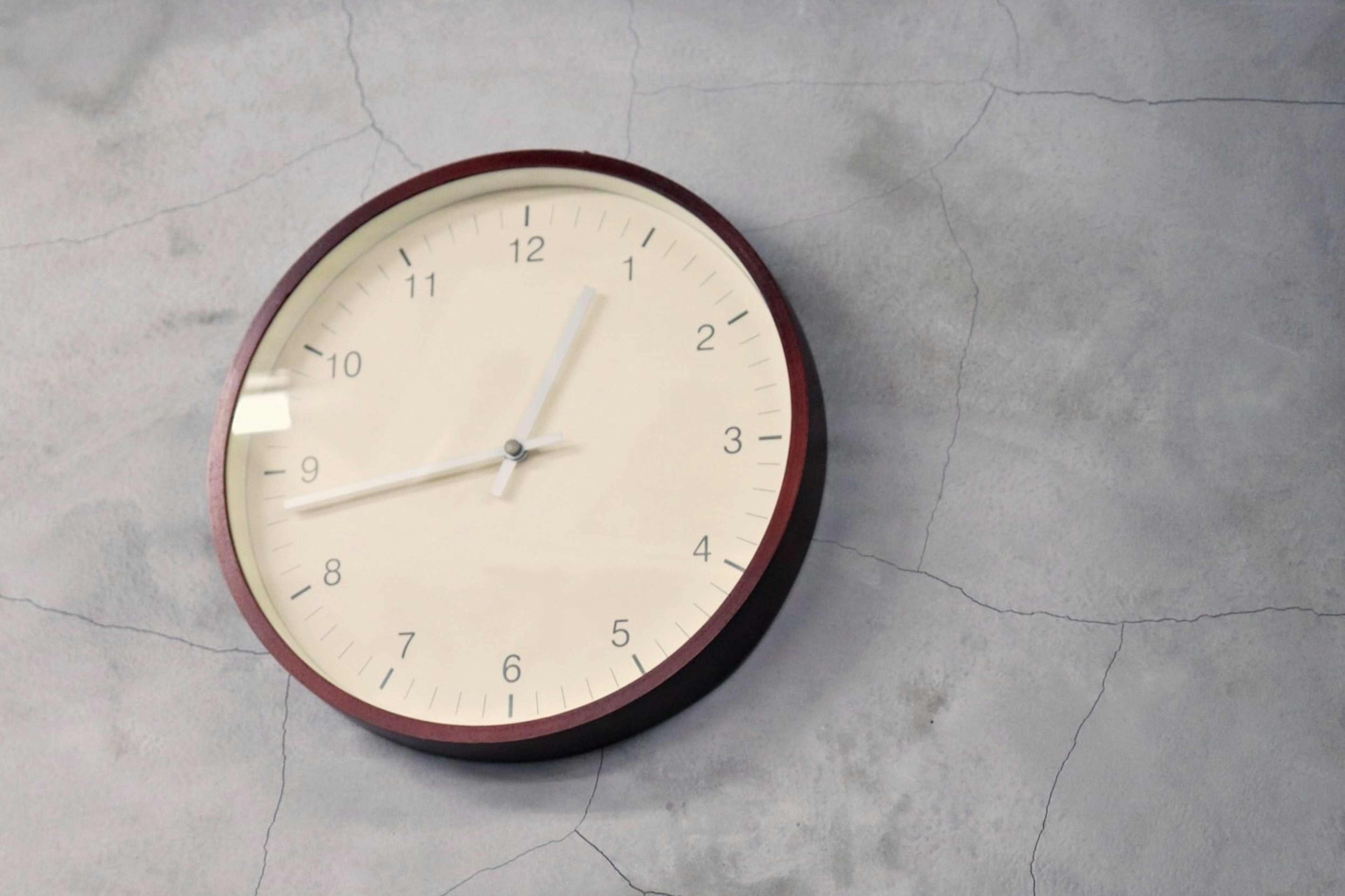 Simple wall-mounted analog clock with a white dial and maroon frame