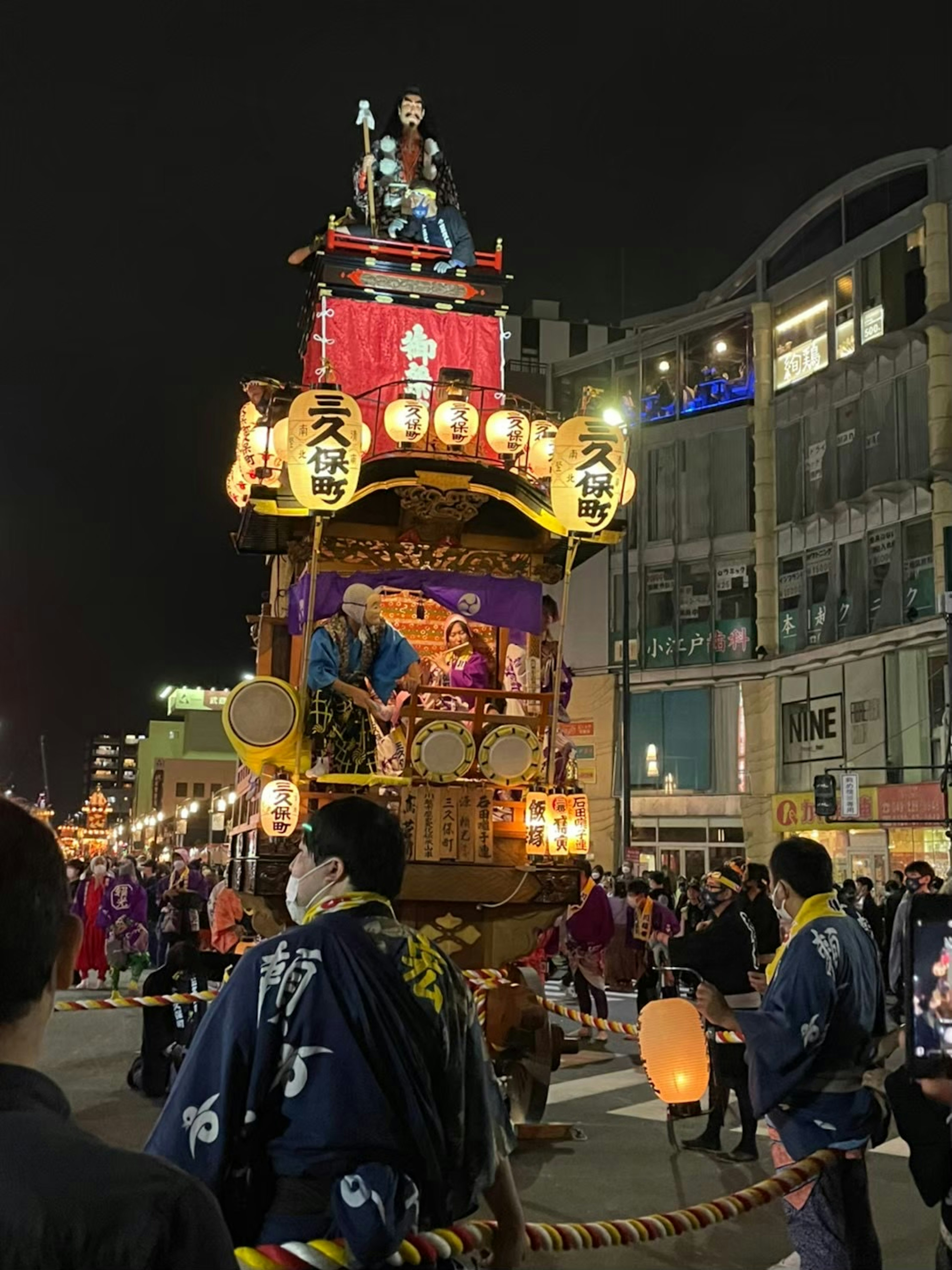 夜の祭りの山車が賑やかな街並みを進む様子