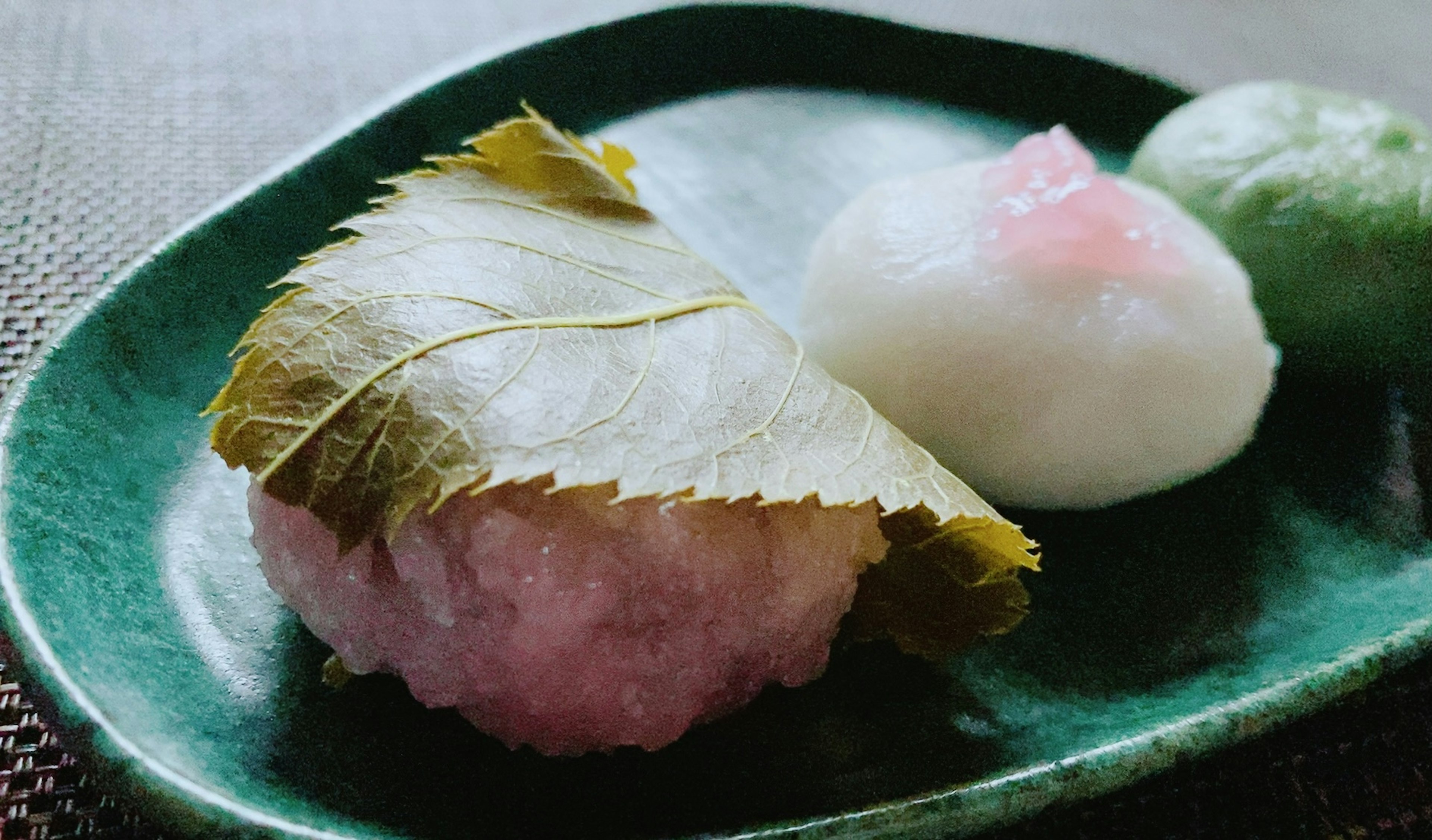 Đĩa xanh với sakura mochi và món tráng miệng Nhật Bản màu trắng