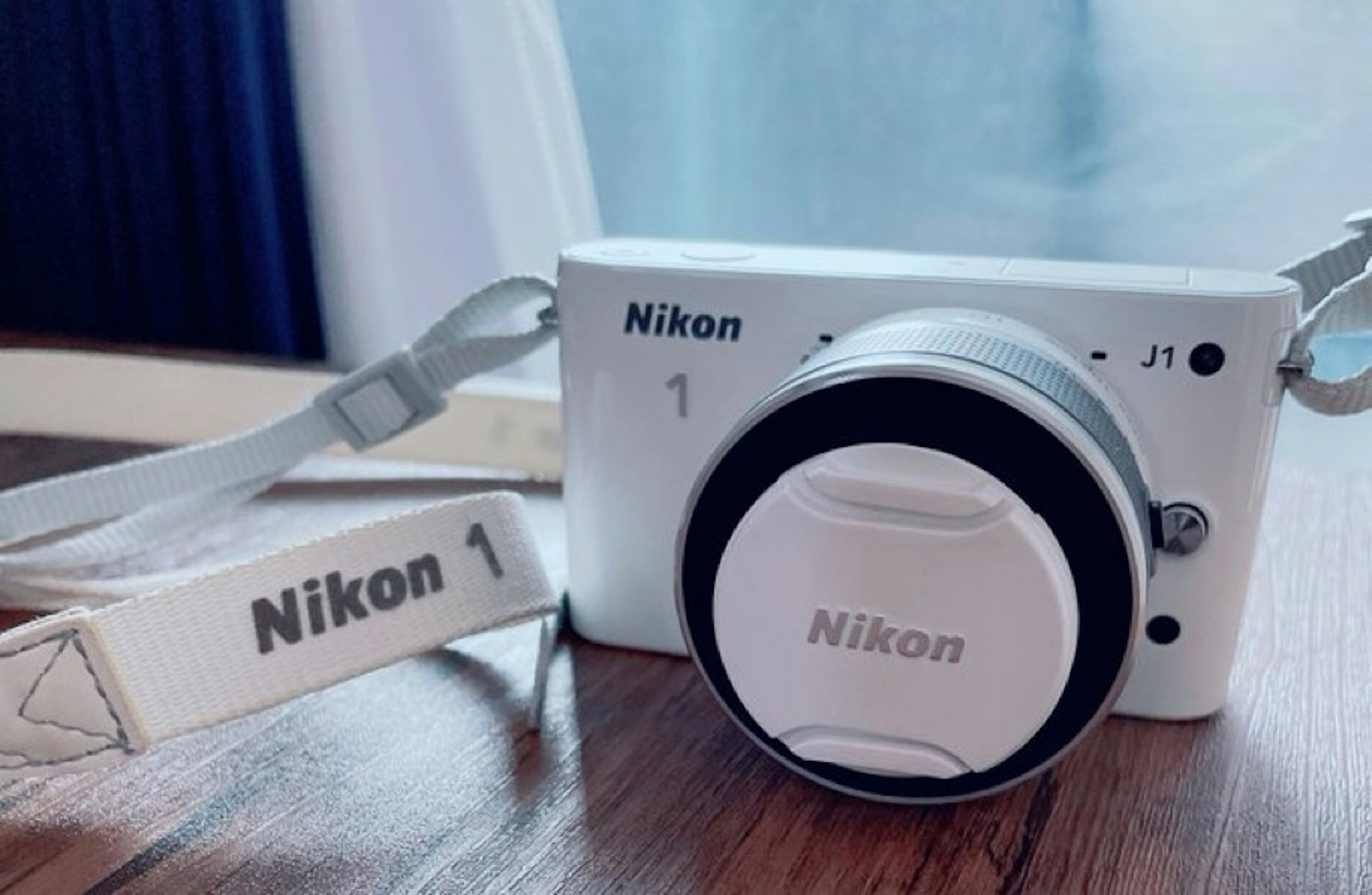 กล้อง Nikon 1 สีขาวพร้อมสายวางอยู่บนโต๊ะไม้