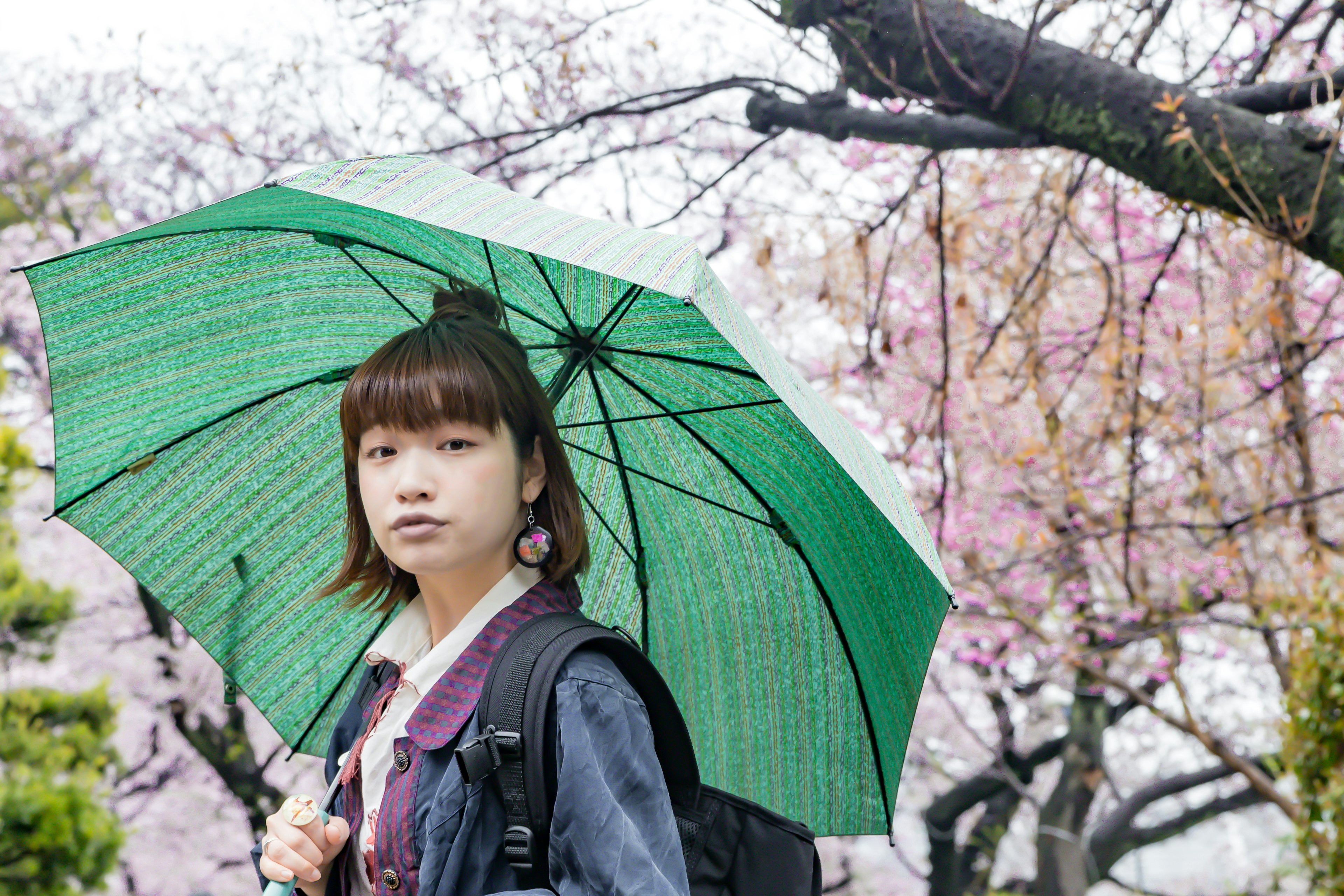 Femme tenant un parapluie vert parmi des cerisiers en fleurs