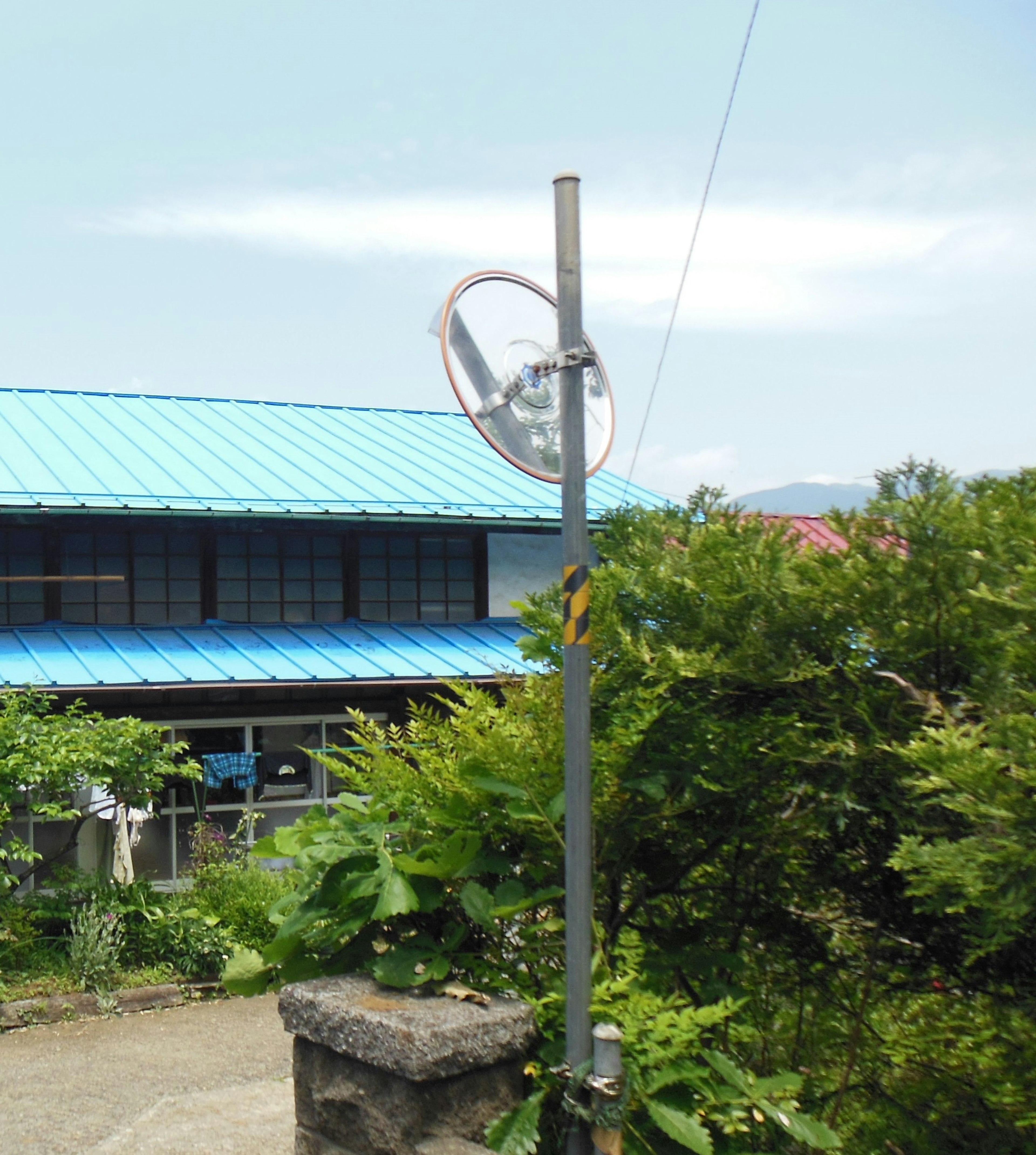 青い屋根の建物と緑の植物がある風景に立つ円形の物体