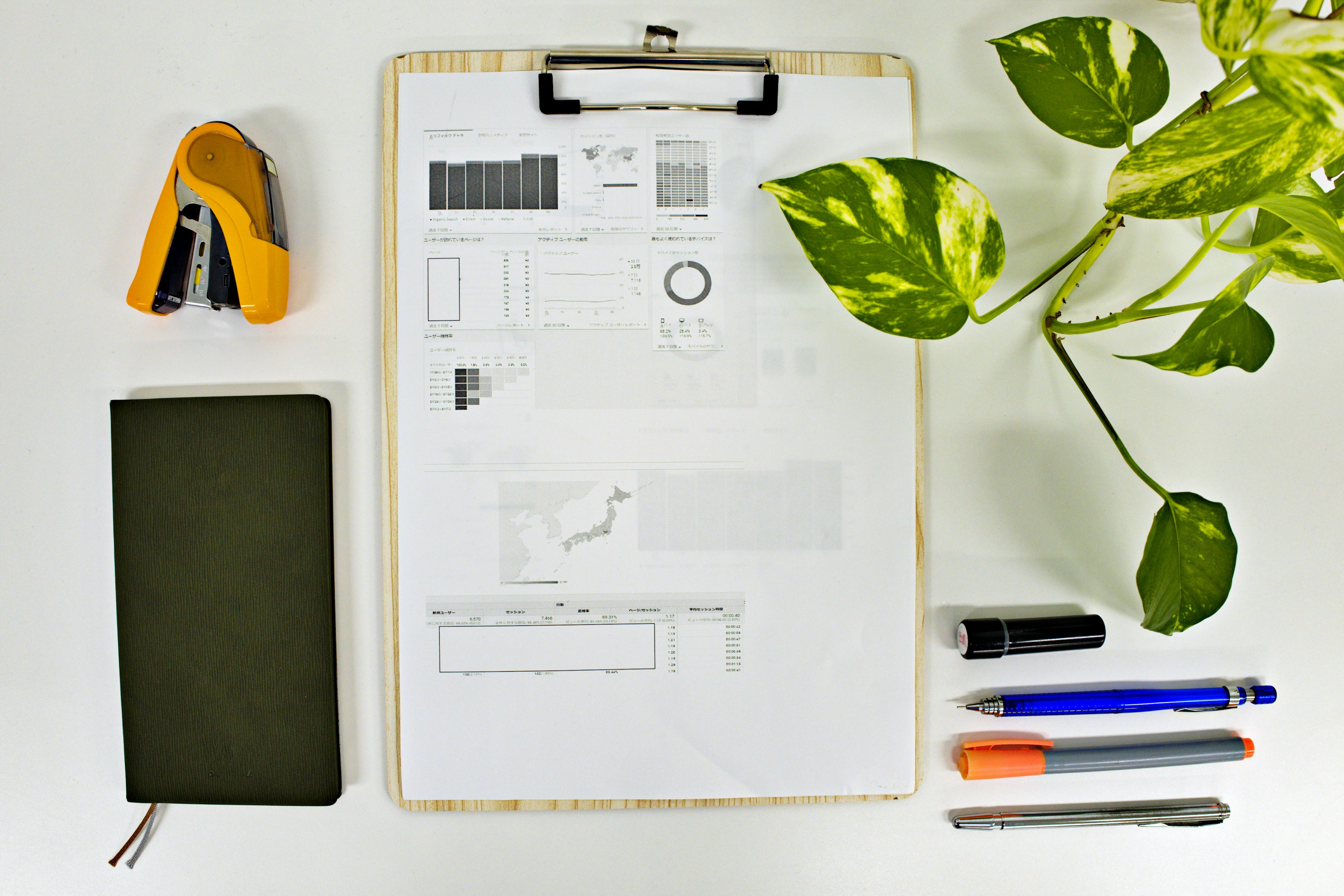 Clipboard with sketches and graphs surrounded by stationery and a plant