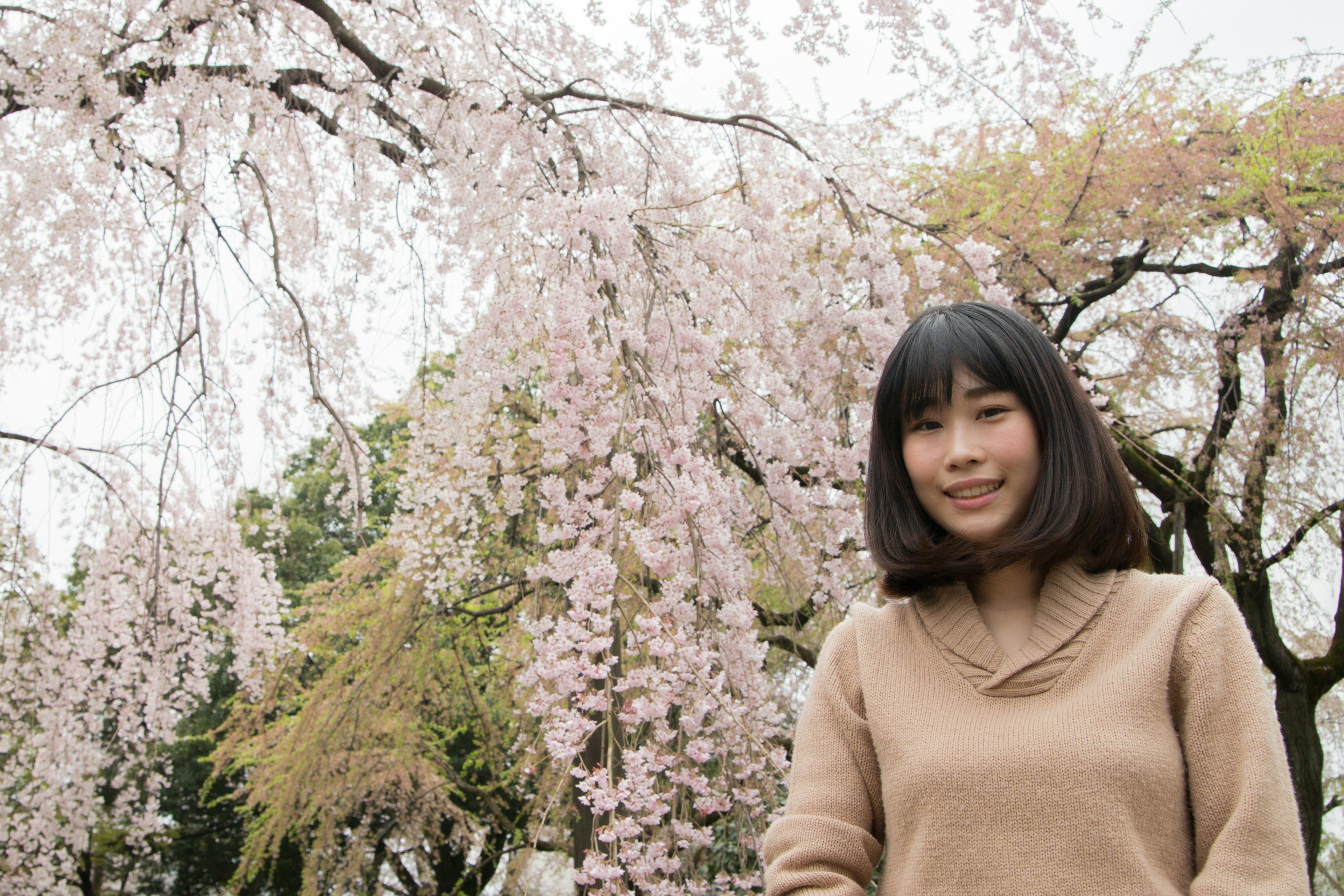 A woman smiling under cherry blossom trees