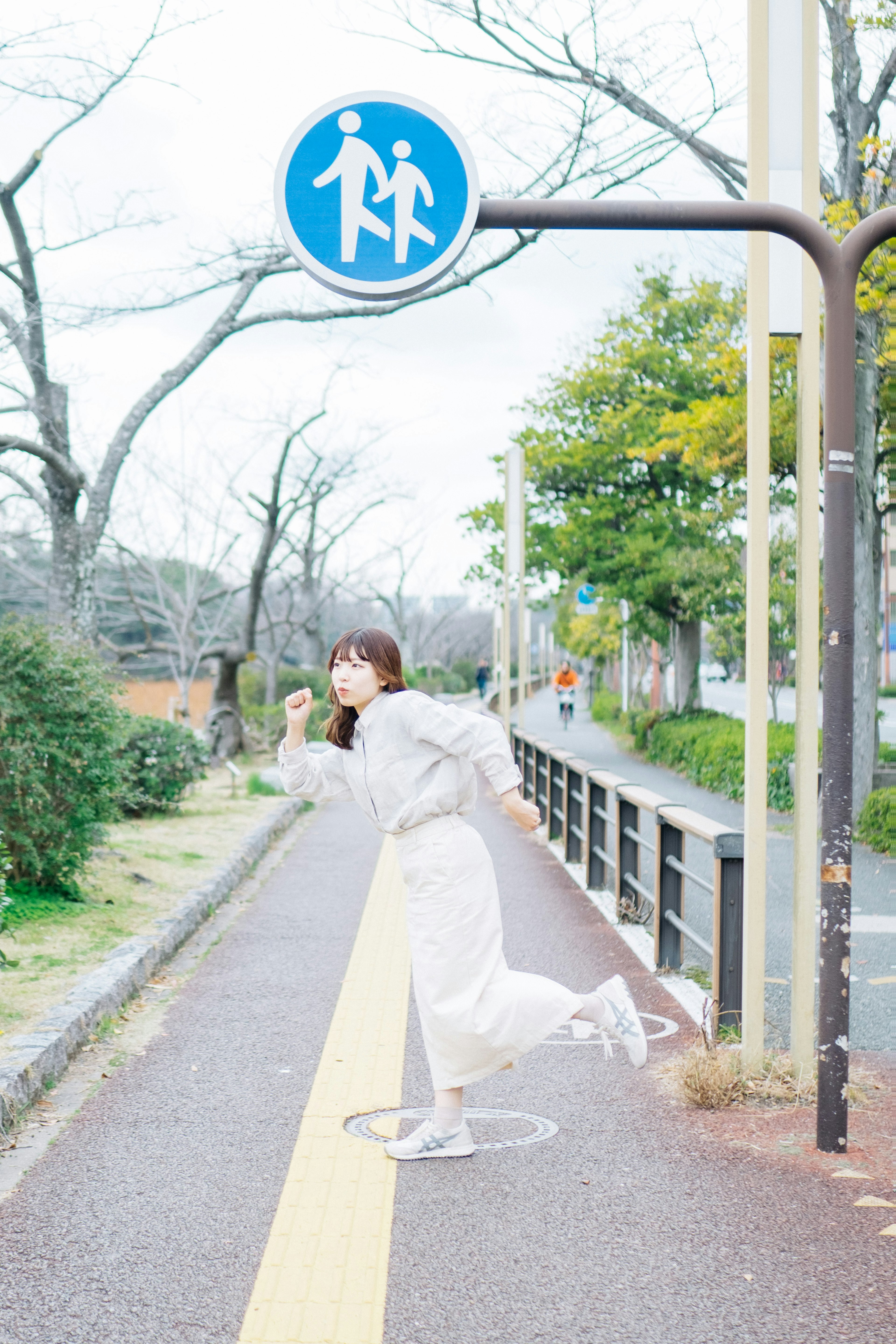 公園の歩道を走る女性の後ろに歩行者の標識がある