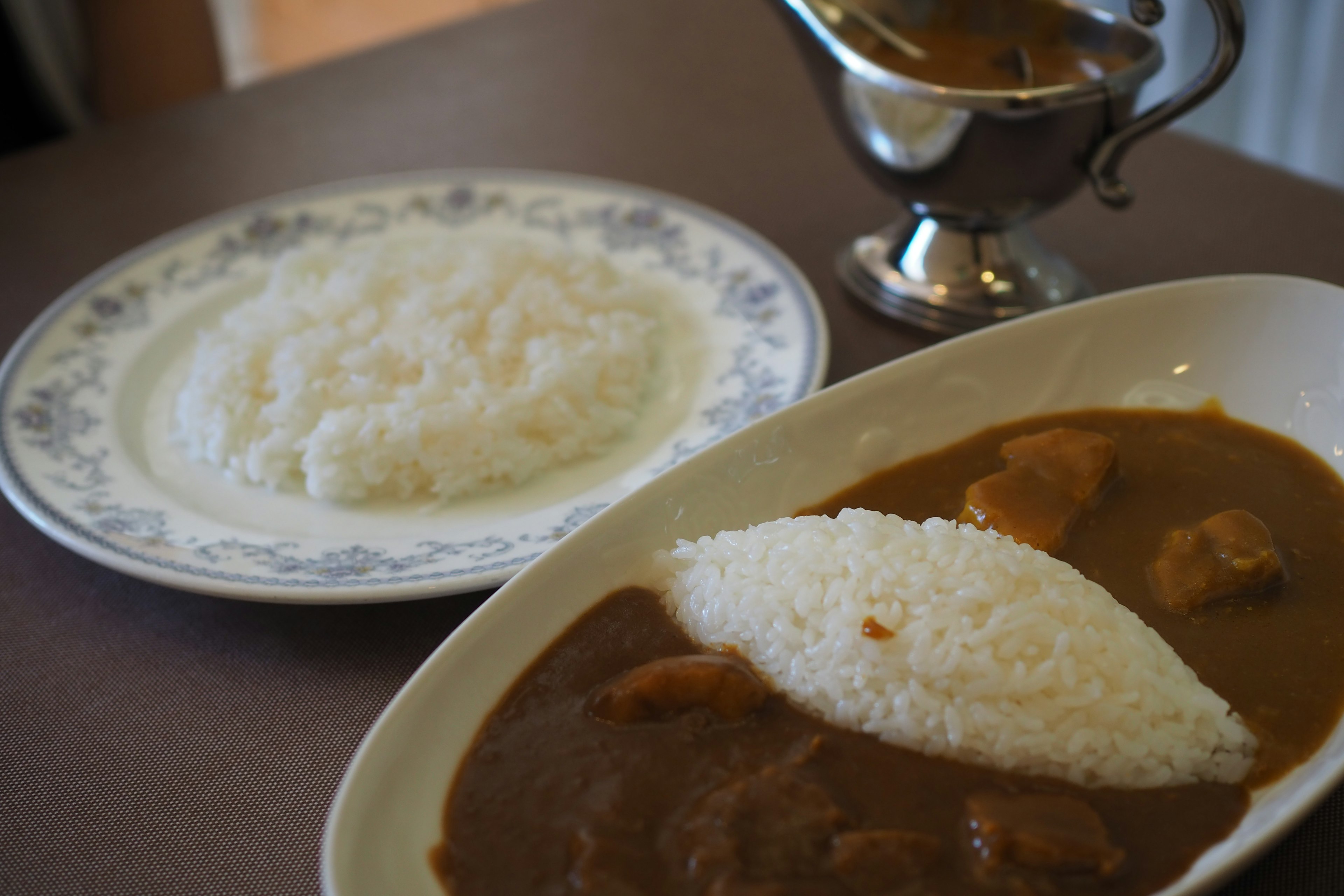 A plate of curry with rice alongside a bowl of plain rice