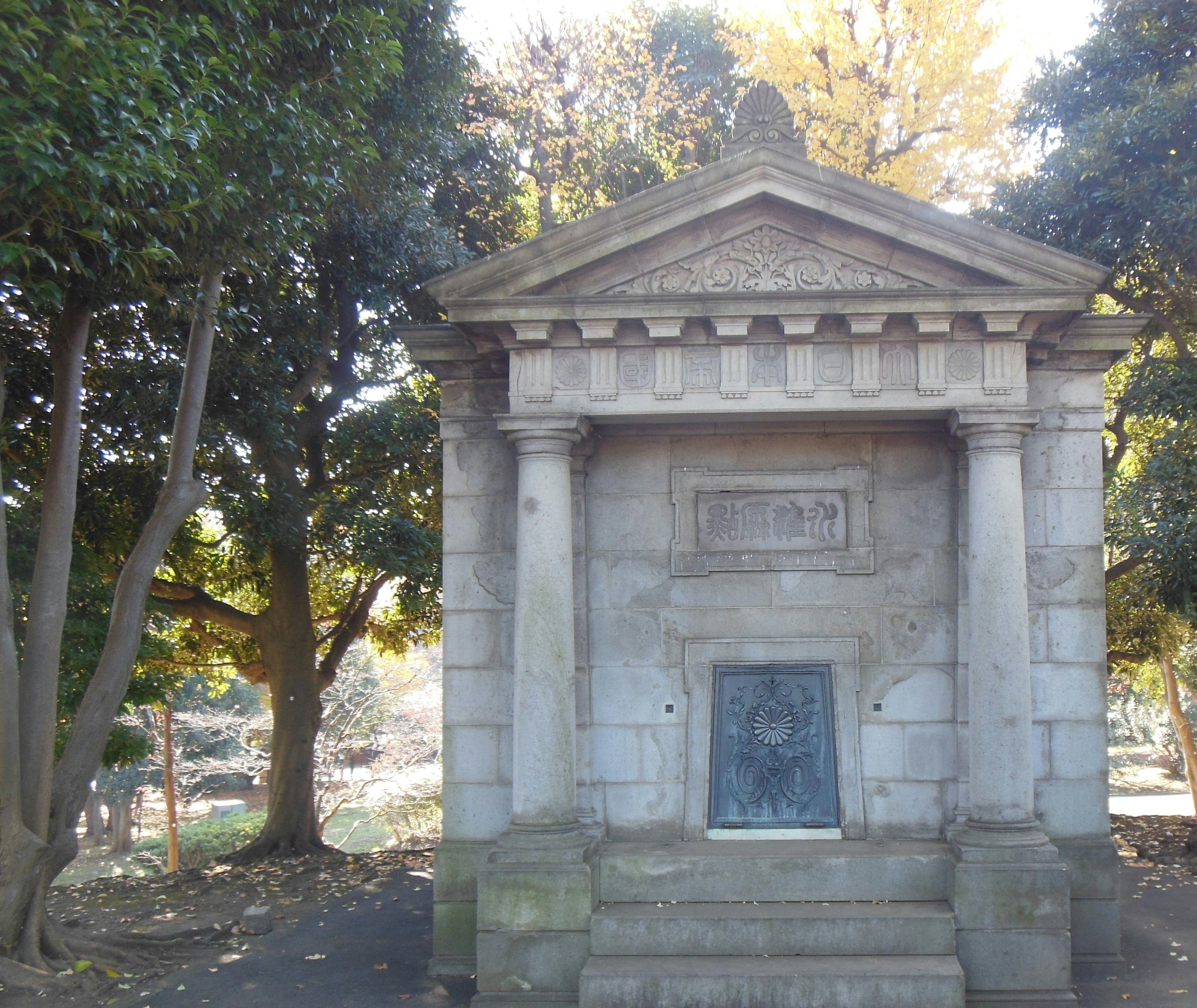 Old stone mausoleum in a historic cemetery surrounded by green trees