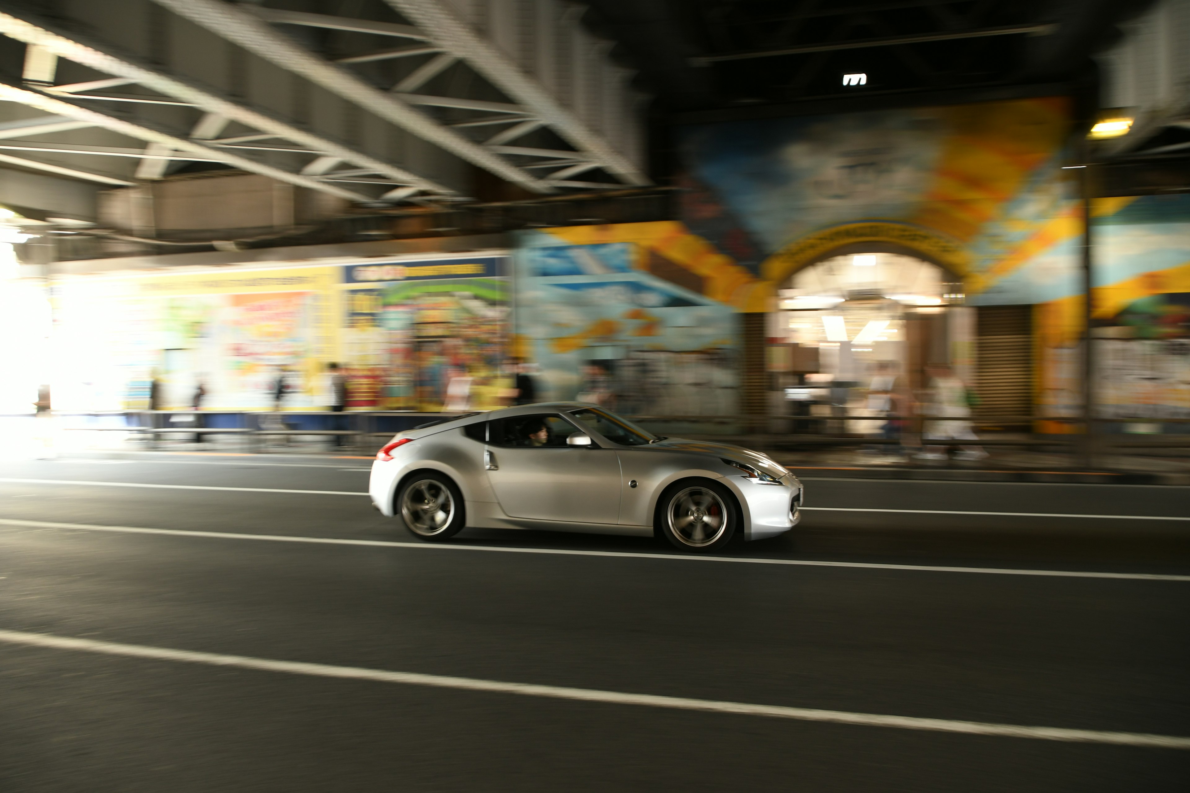 A silver car passing through an archway tunnel with colorful murals in a city setting