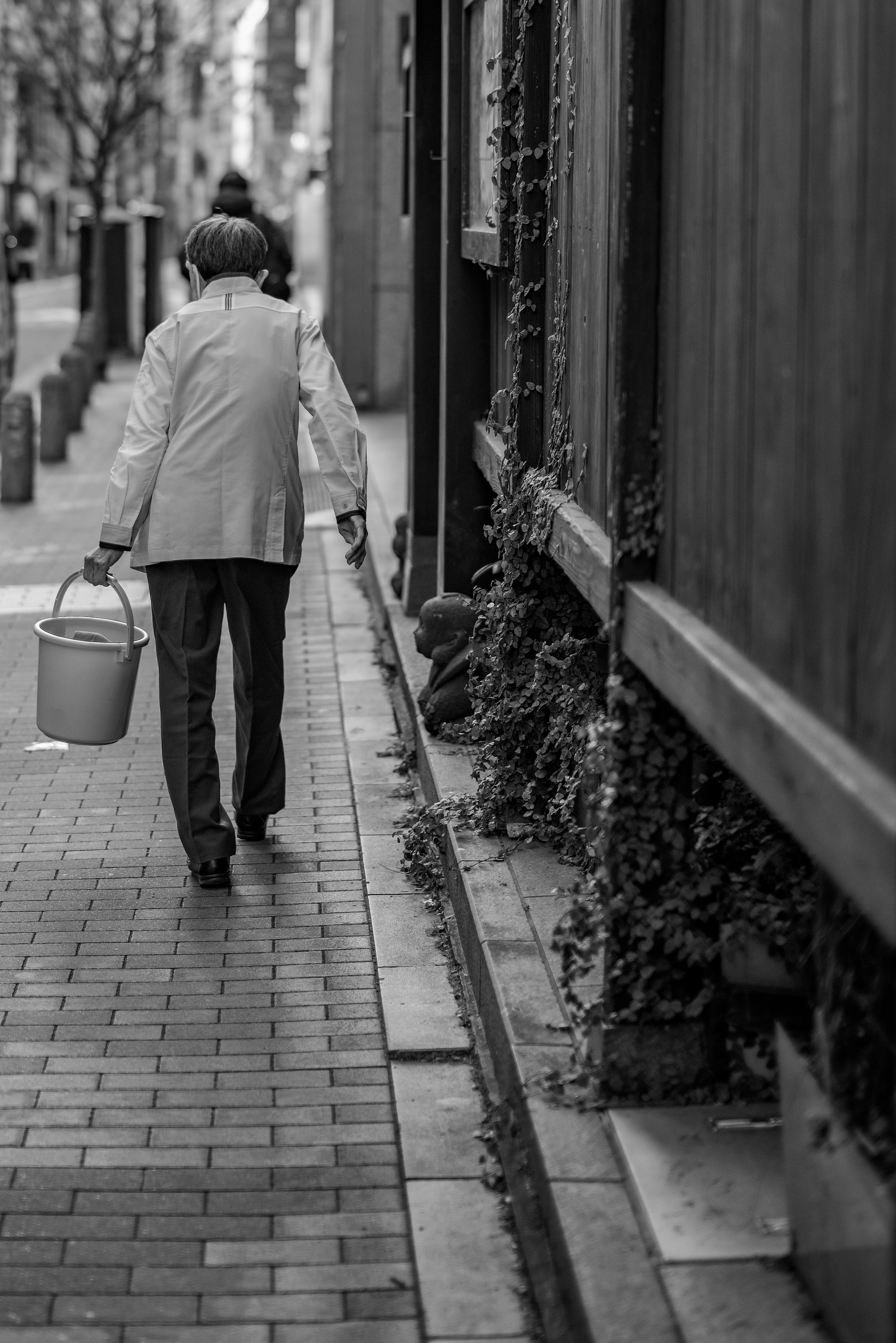 Une personne marchant dans une rue en noir et blanc avec un seau