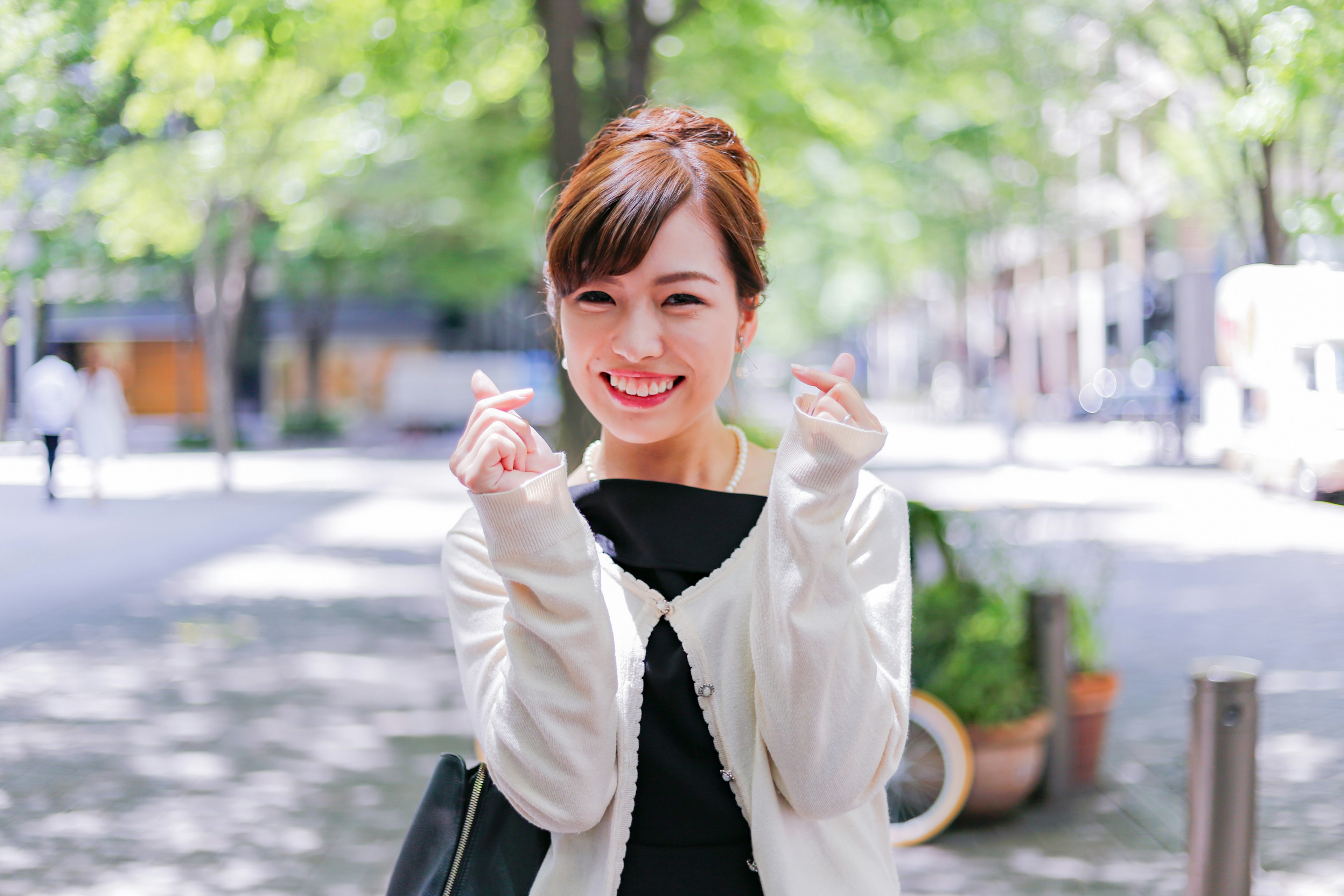 Young woman smiling and making heart gesture in a lush green street