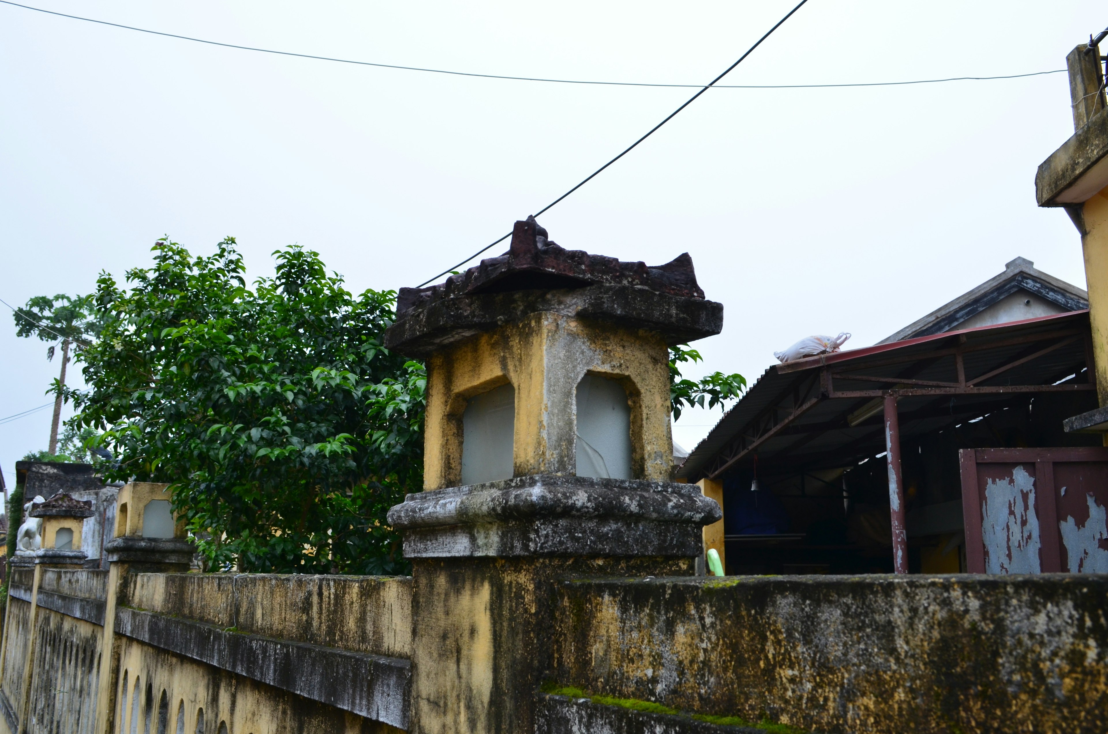 Stone pillars near an old wall and a building with a roof