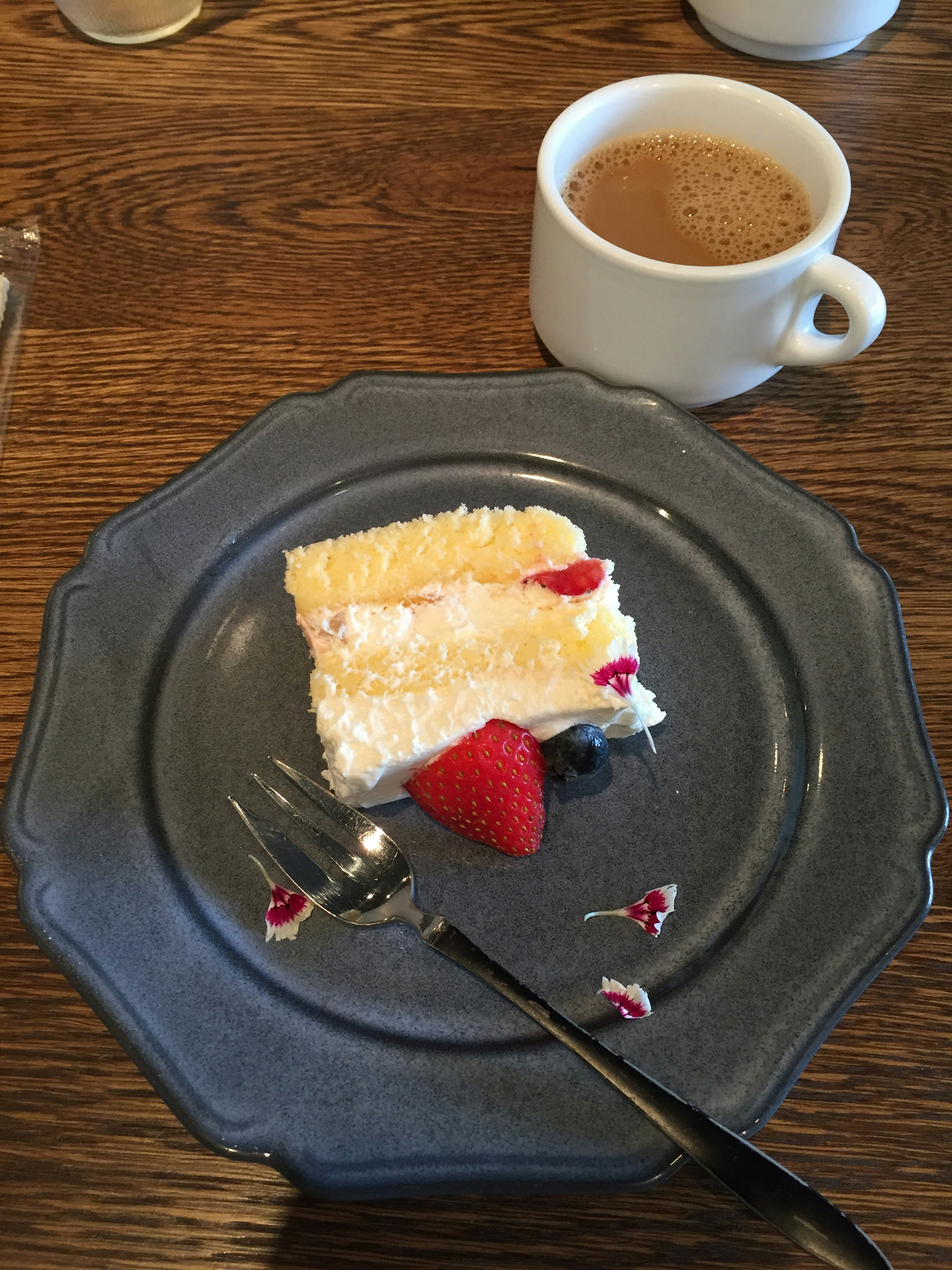 A slice of lemon cake with strawberries on a blue plate next to a cup of coffee