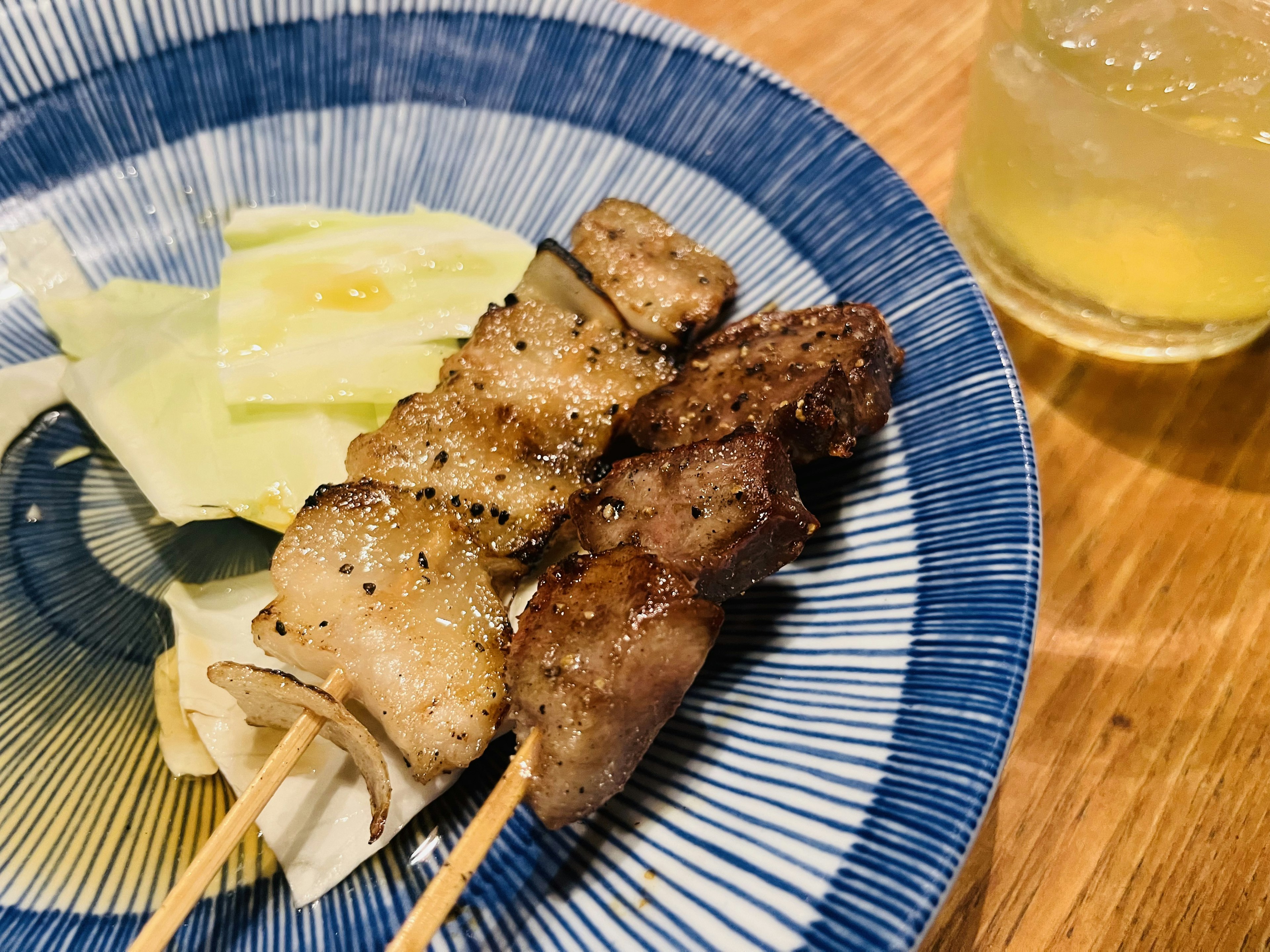 焼き鳥の串がある青い皿にキャベツと飲み物