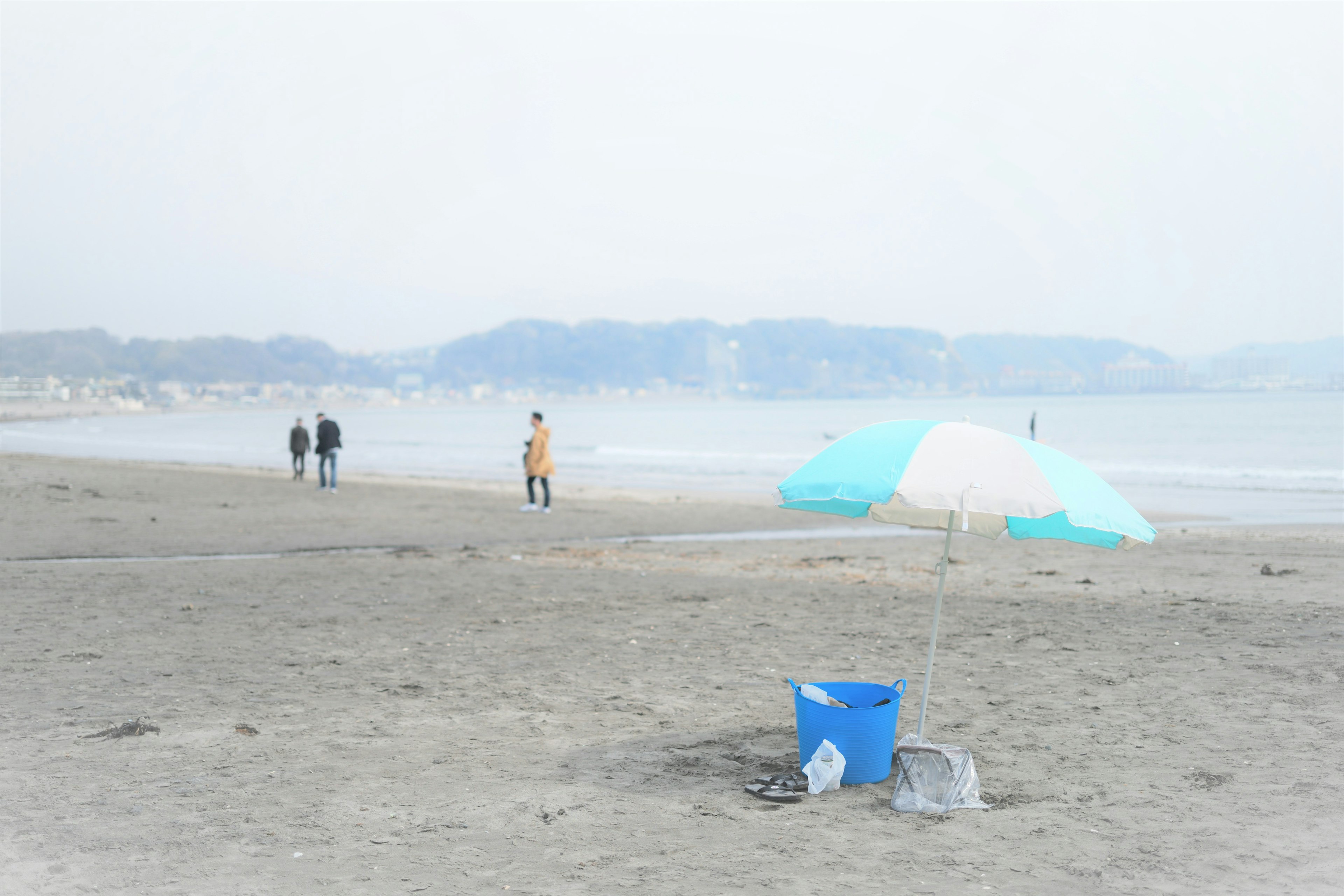 Scena di spiaggia nebbiosa con persone che camminano e un ombrellone colorato