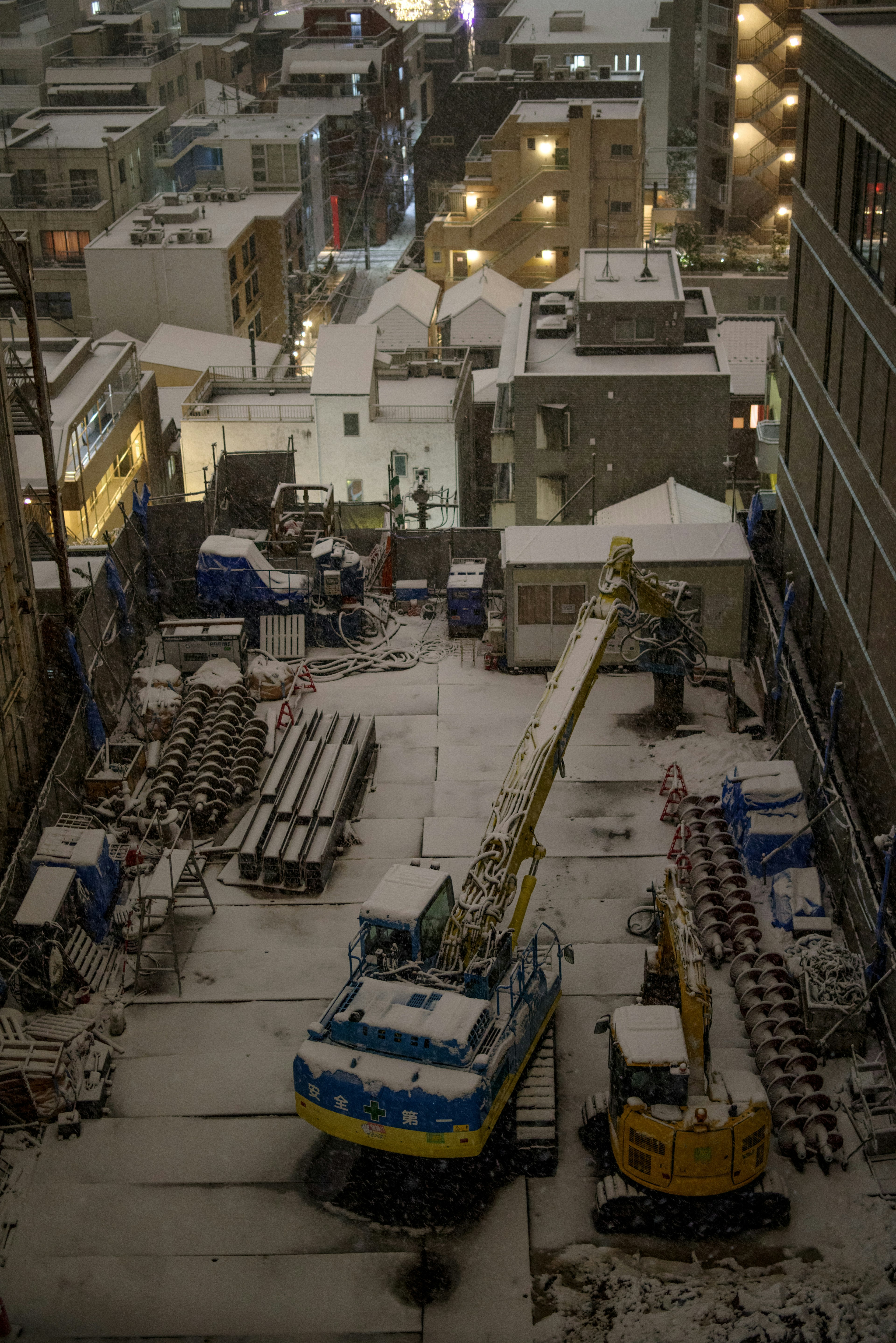 Construction site in a snowy urban setting featuring machinery and materials