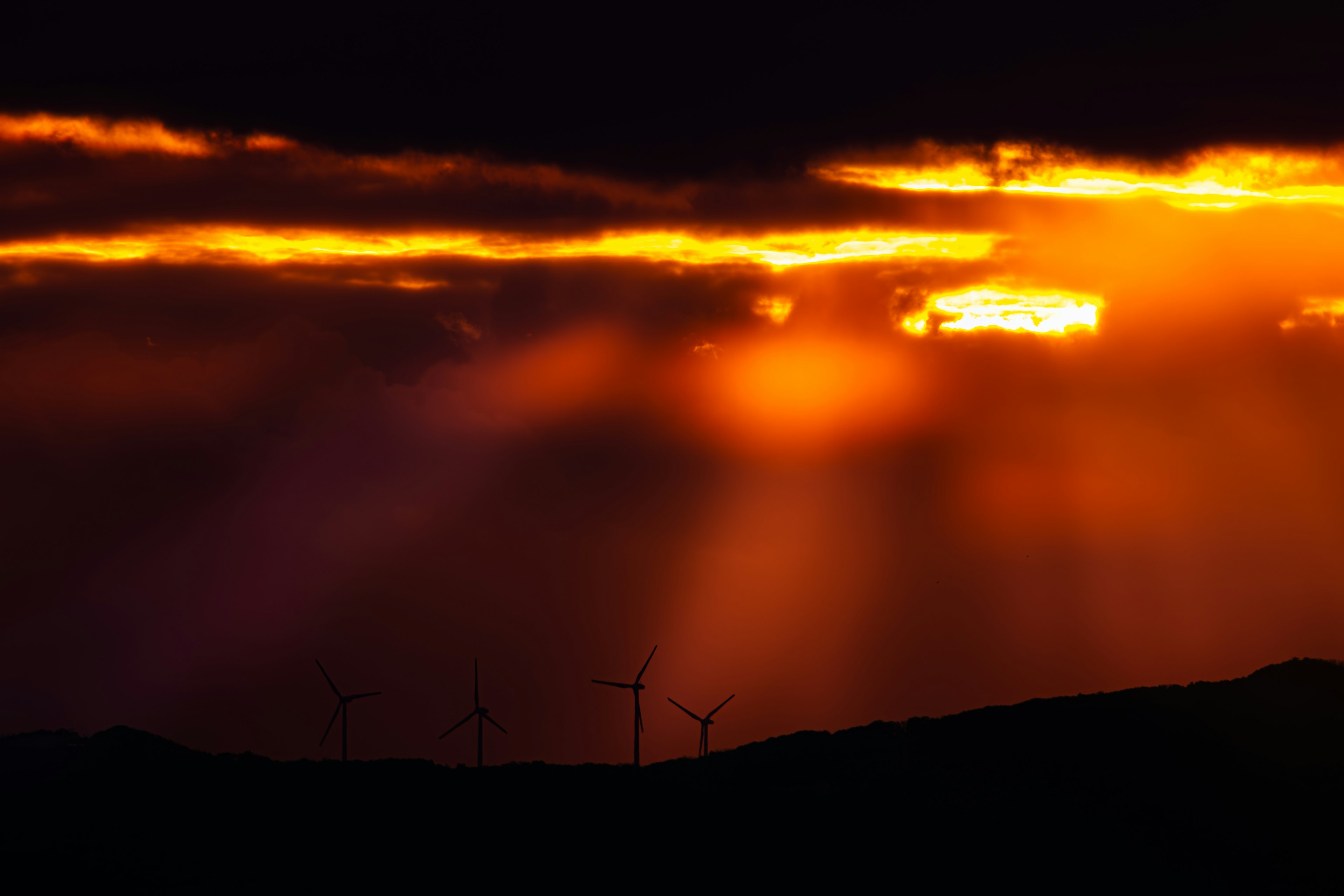 Vibrant orange sunset illuminating clouds with silhouetted wind turbines