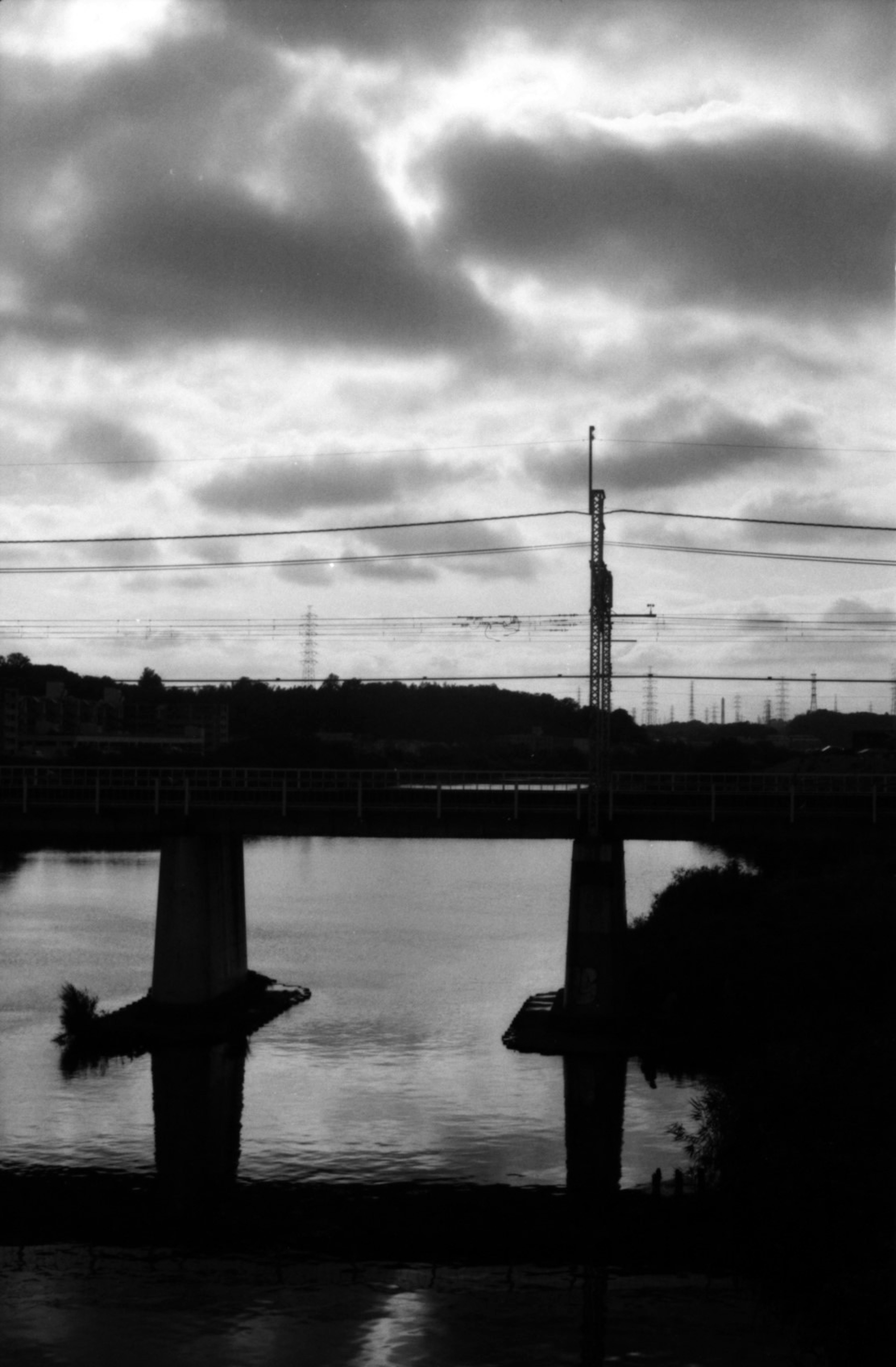 Schwarzweißbild einer Brücke über einen Fluss mit tiefen Wolken und Reflexionen auf dem Wasser