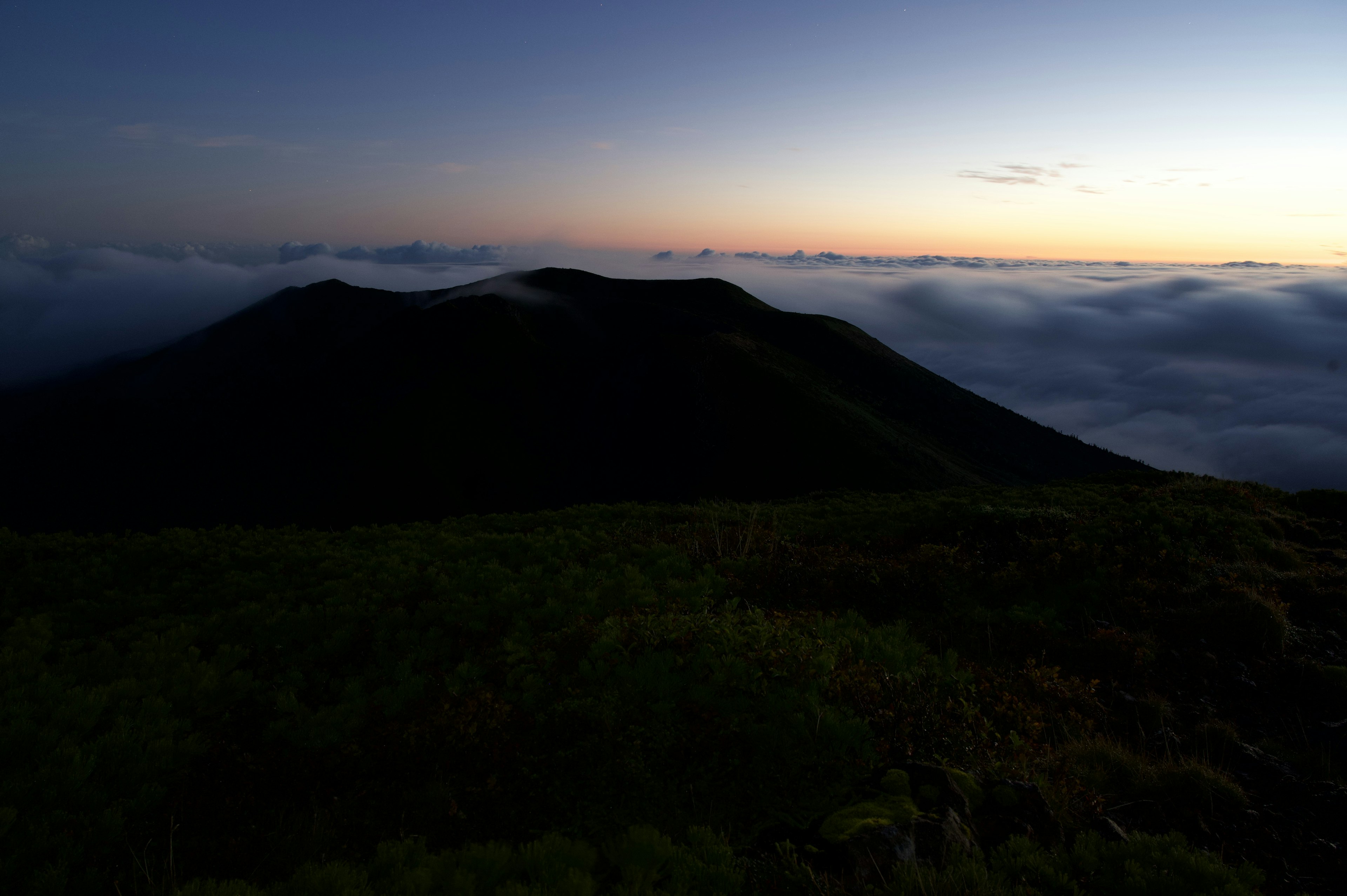 雲海の上にそびえる山のシルエットと薄明かりの風景