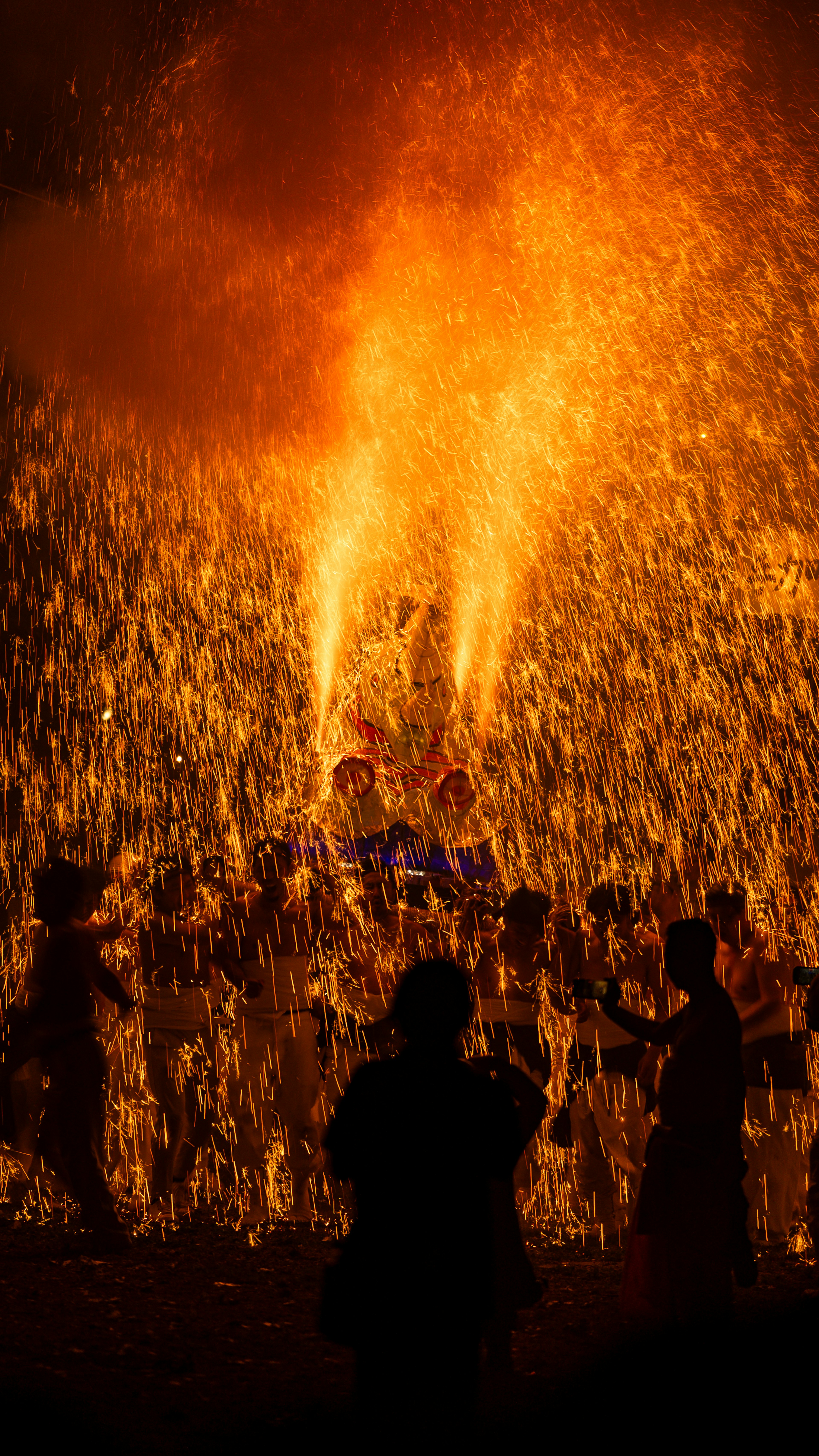 Festivalszene mit Menschen, die zwischen Flammen und Silhouetten tanzen