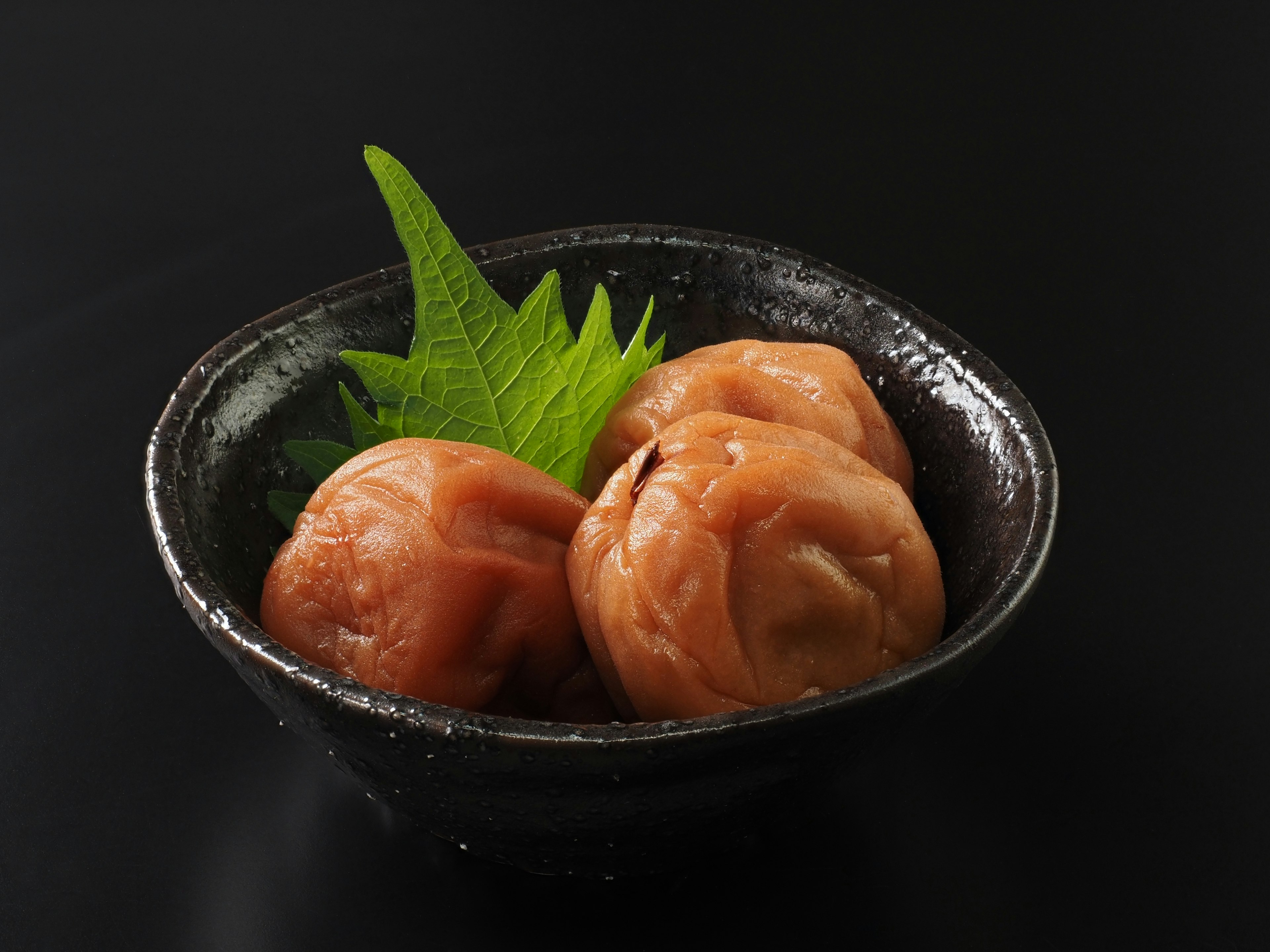 Pickled plums served in a black bowl with shiso leaves