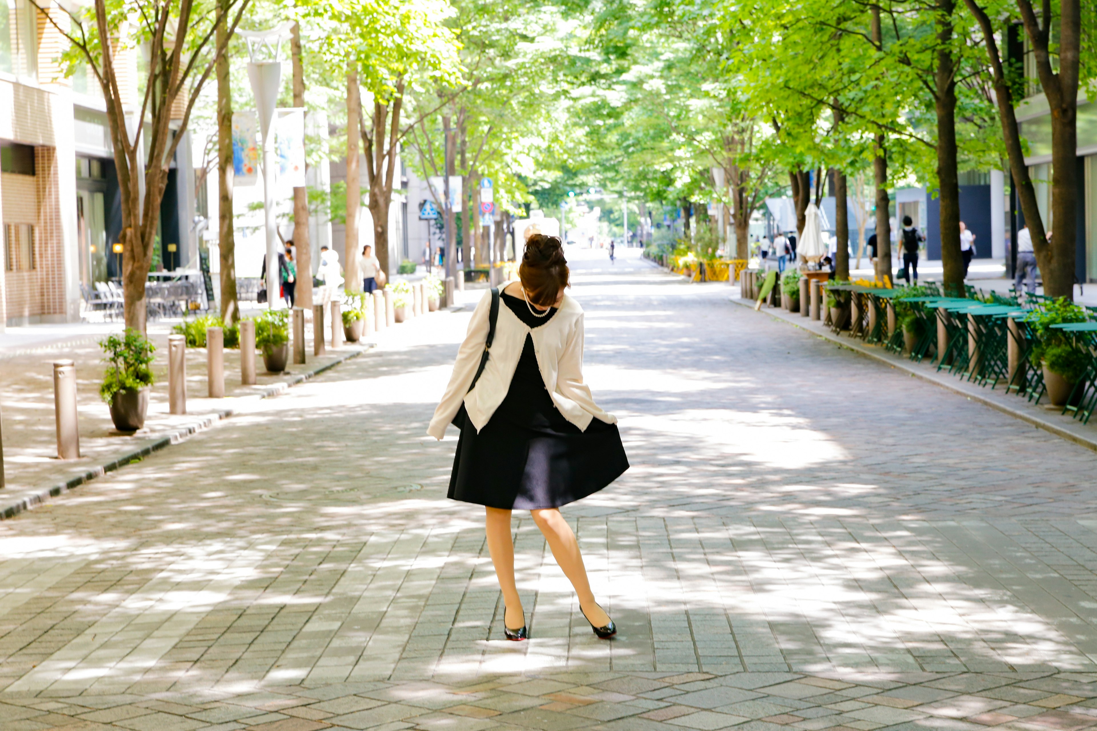 Une femme en robe noire marchant dans une rue calme entourée d'arbres verts