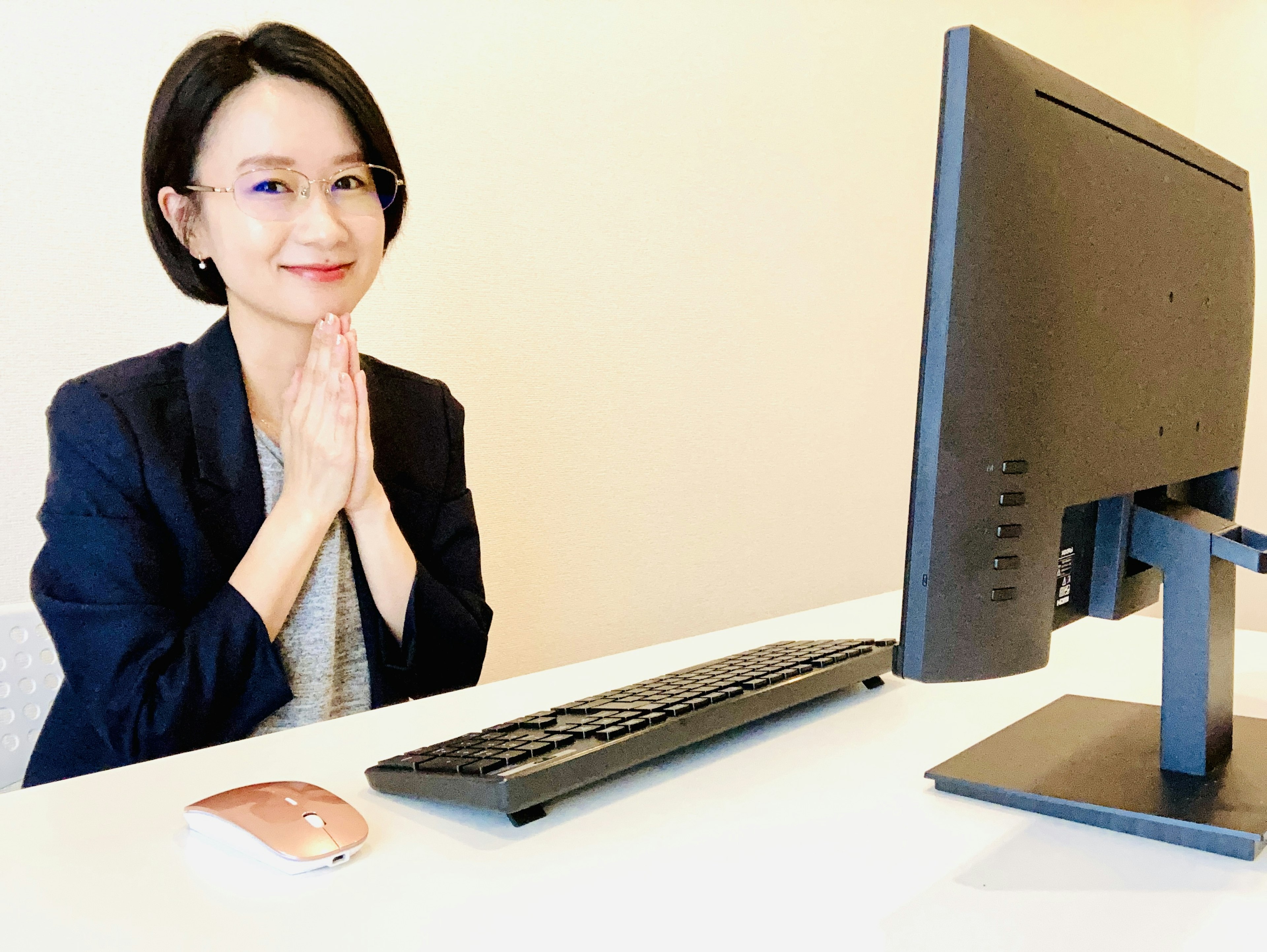 A woman smiling with hands clasped at a desk with a computer