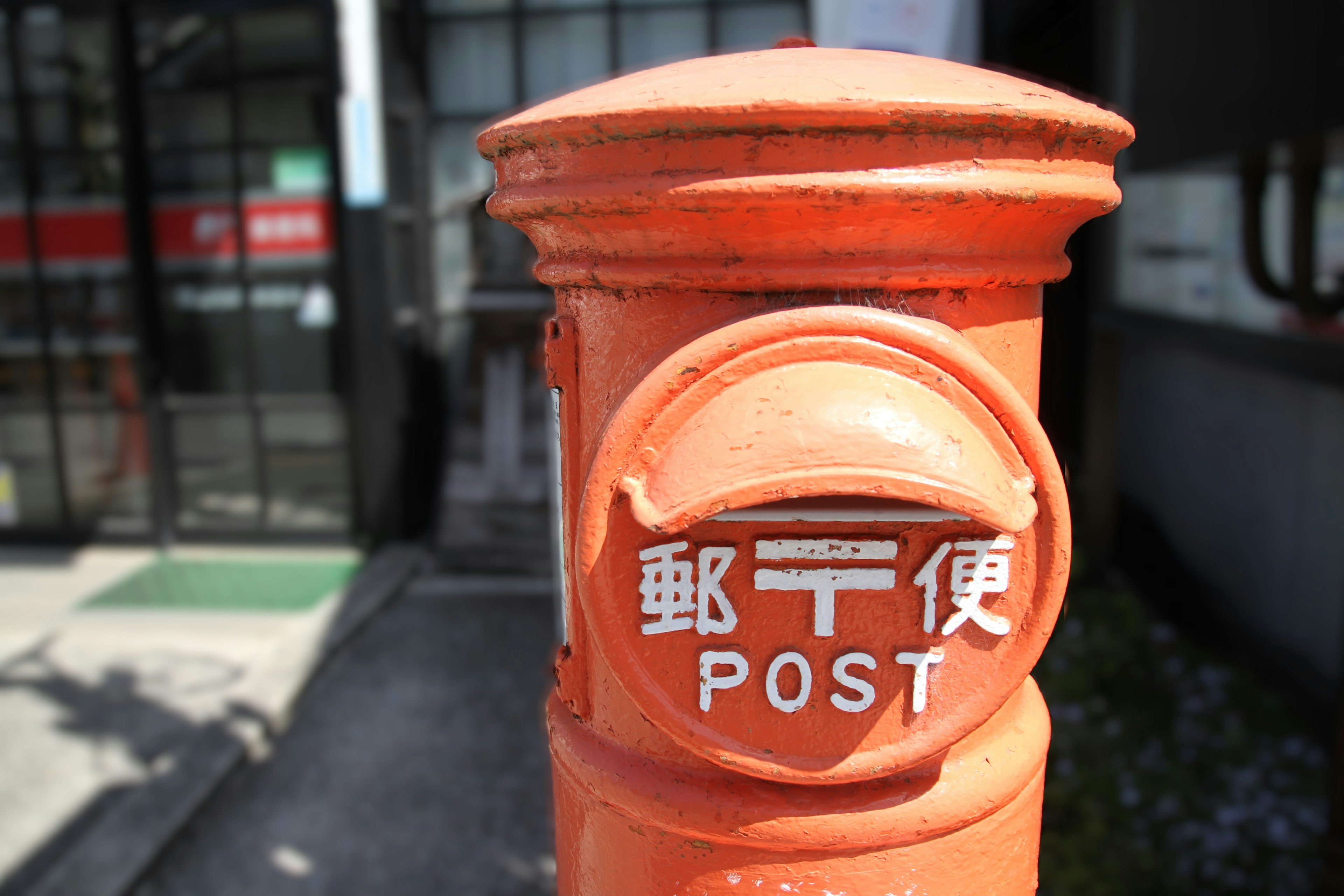 Oranger Briefkasten mit japanischen Zeichen für Post und dem Wort POST