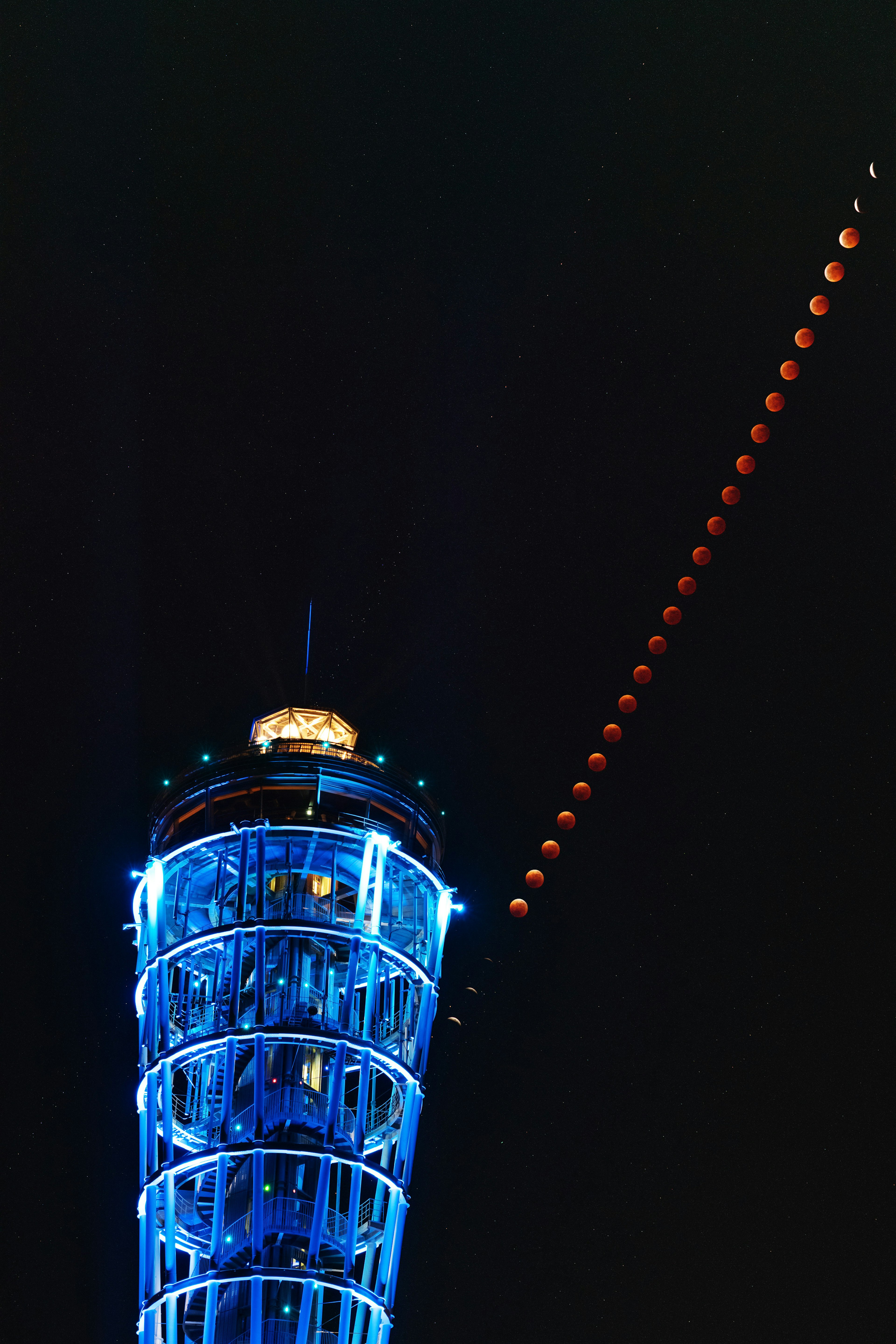 Alto torre illuminata di blu con una serie di lune rosse nel cielo notturno