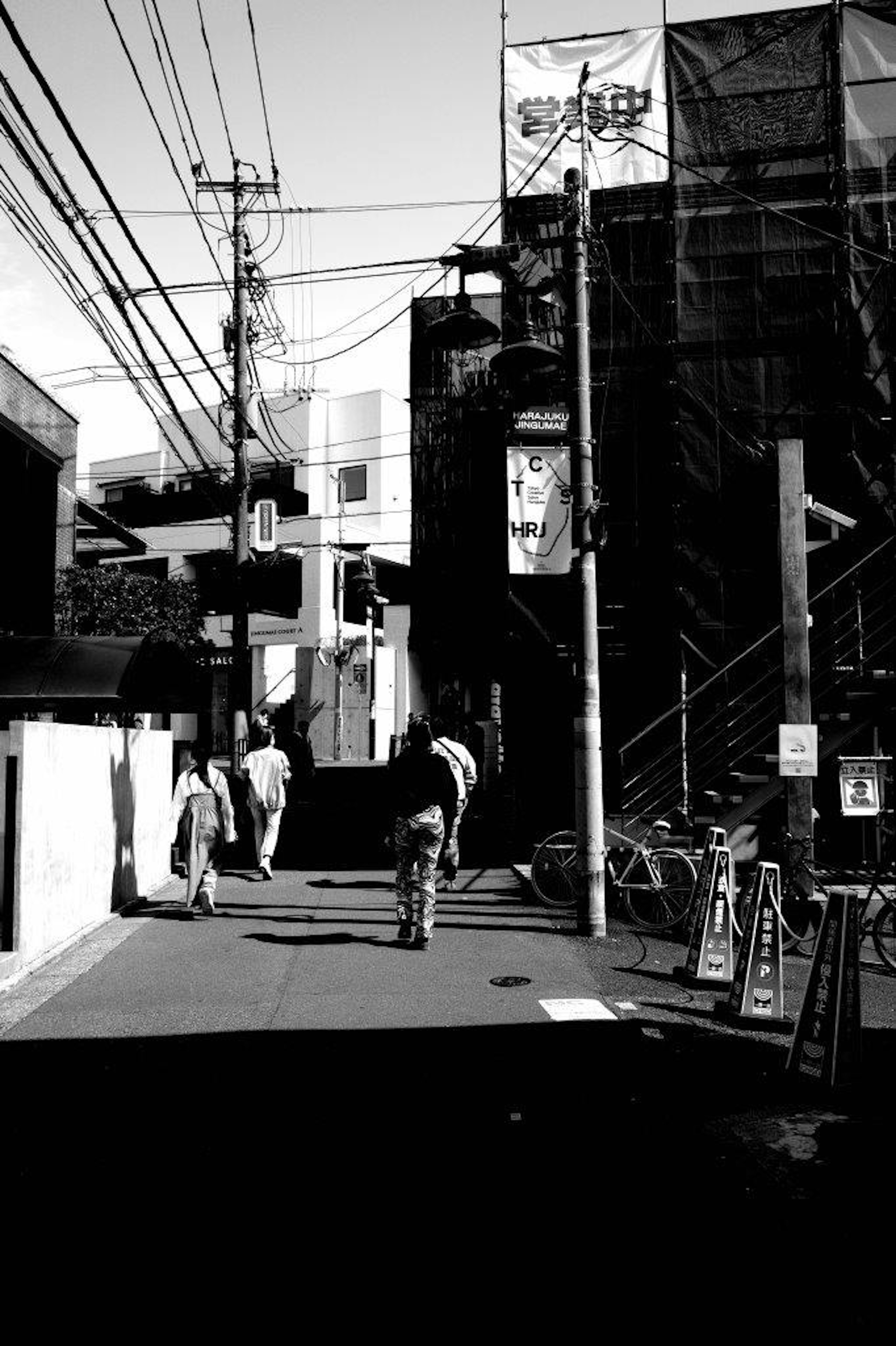 Scène urbaine en noir et blanc avec un cycliste et des piétons bâtiments et lignes électriques visibles