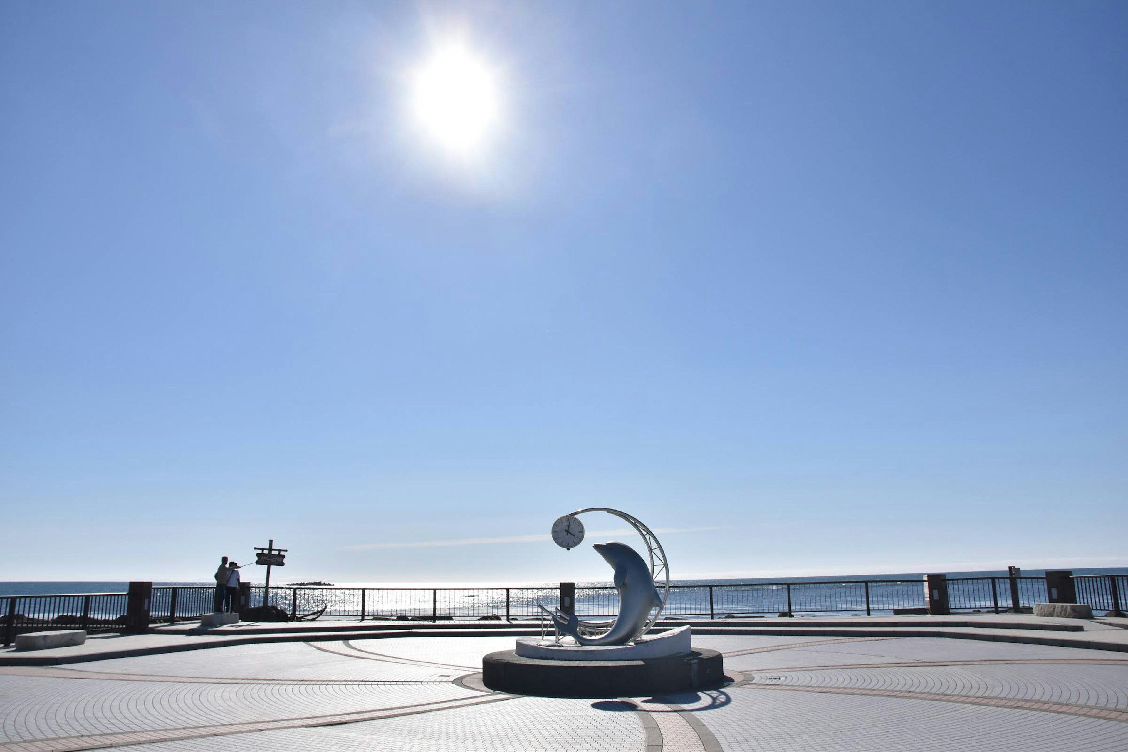 Escultura junto al mar bajo un cielo azul claro con sol brillante