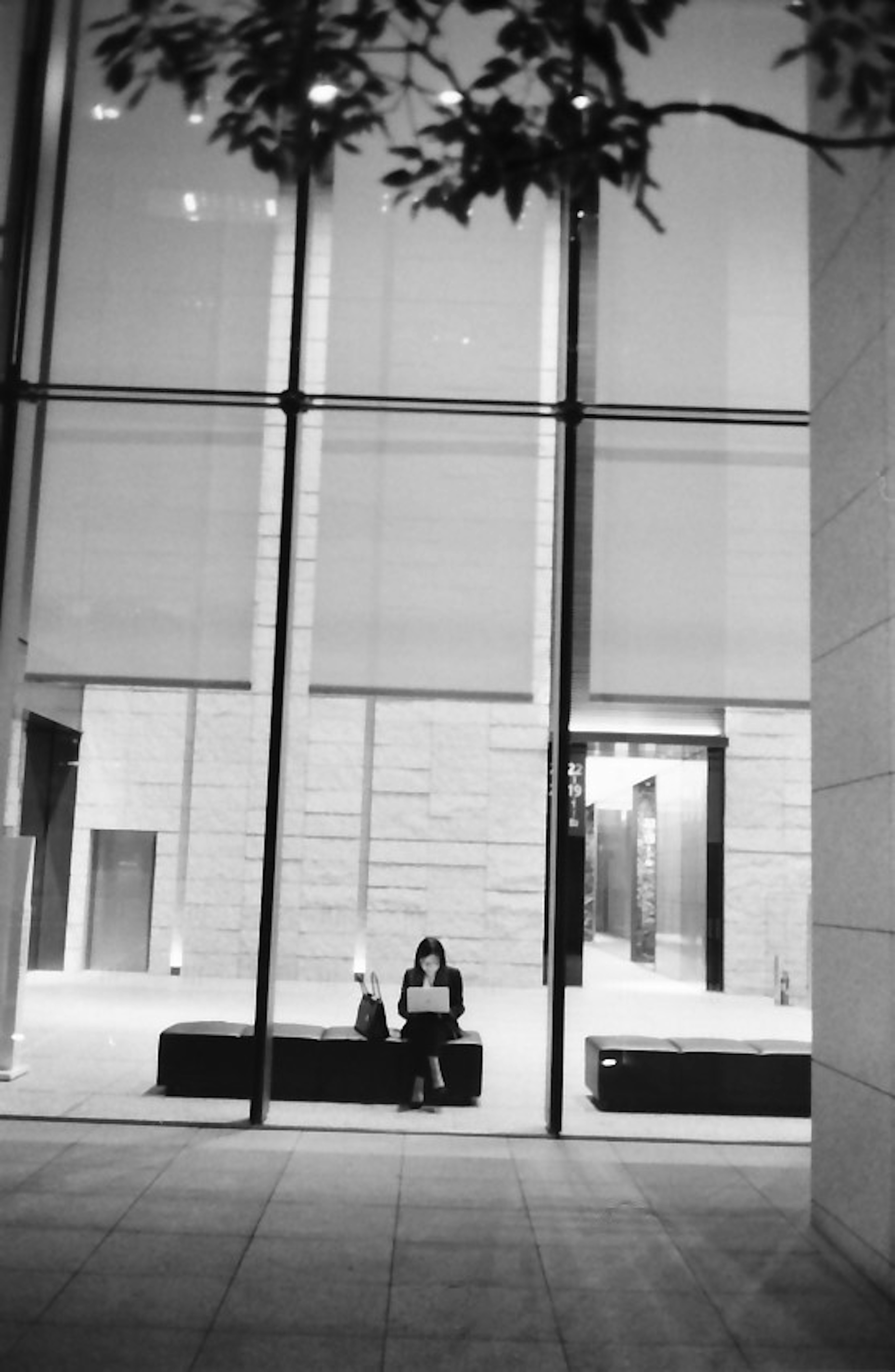 Une femme assise devant de grandes fenêtres en verre dans un bâtiment moderne avec un intérieur simple