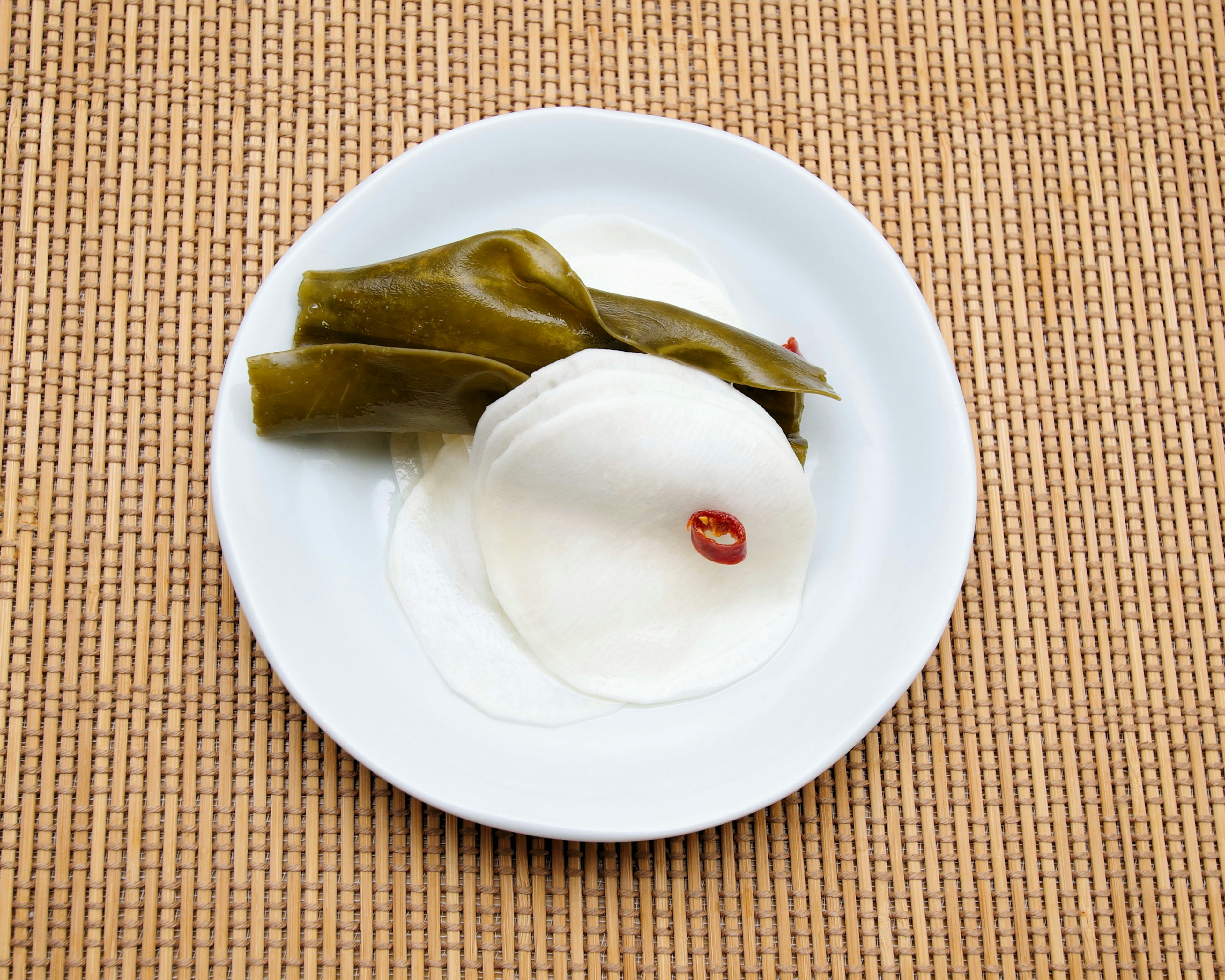 Pickled radish and green leaf vegetables on a white plate