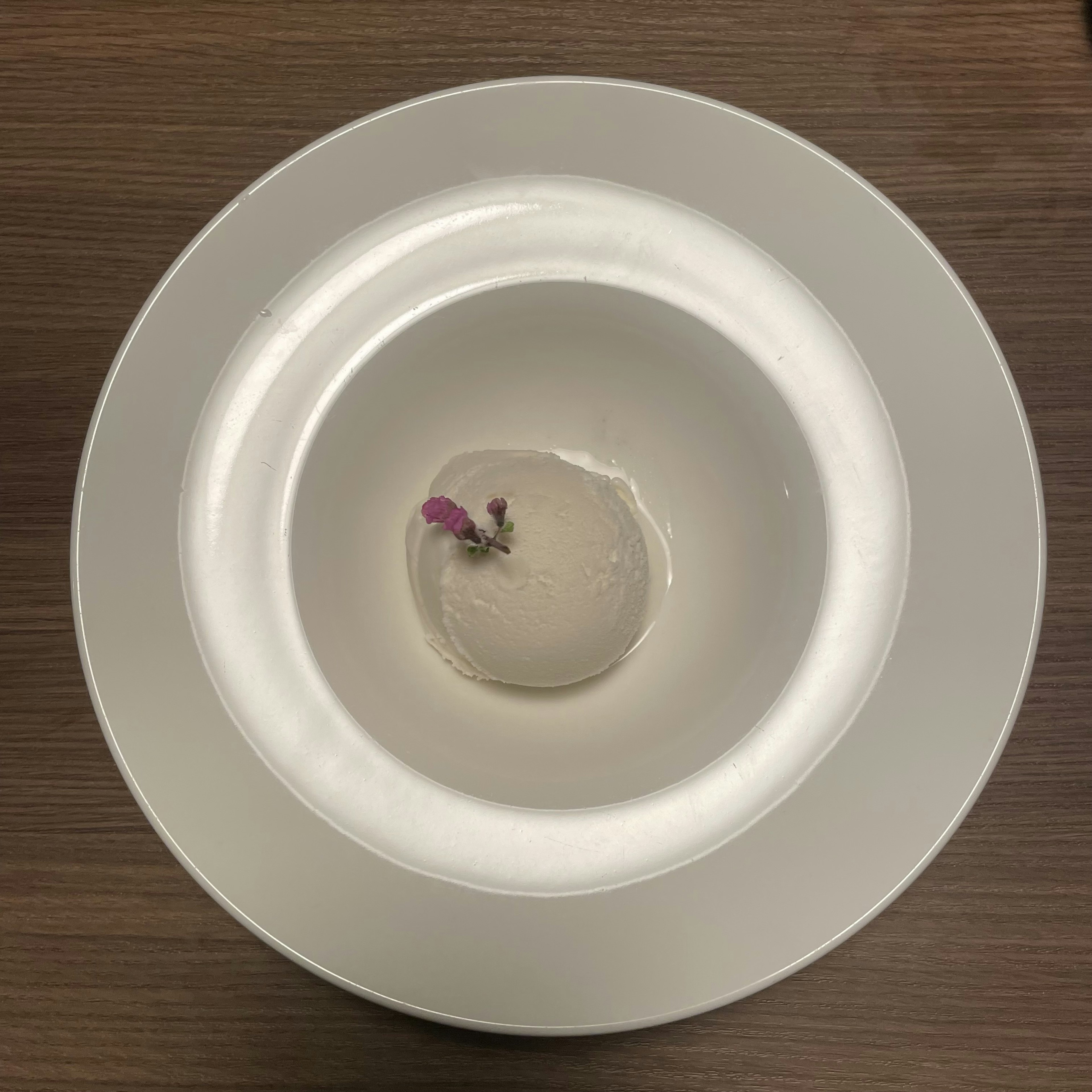 Una pequeña esfera transparente con un trozo de flor colocado en el centro de un plato blanco