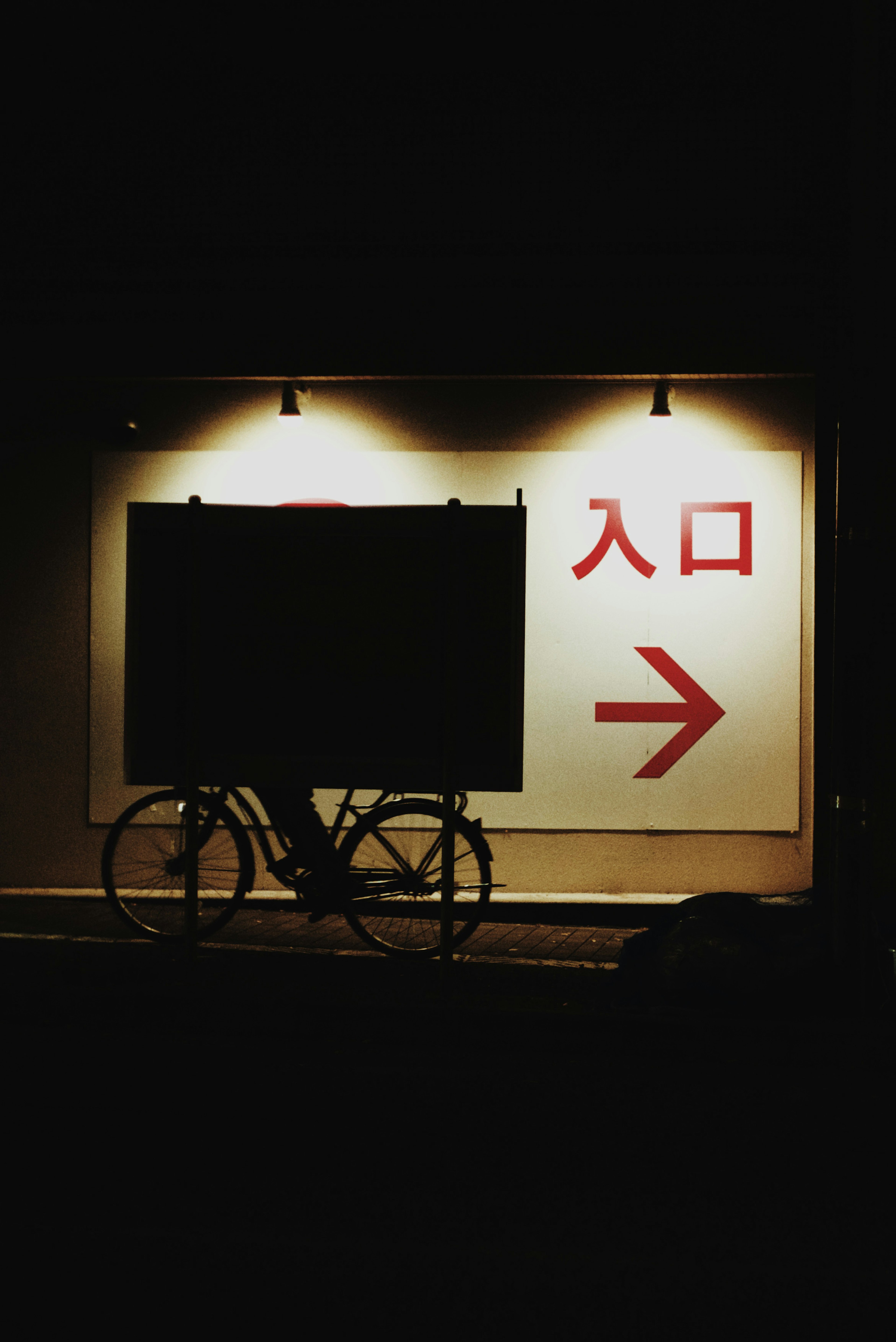 A black bicycle in front of a wall with a red arrow and entrance sign