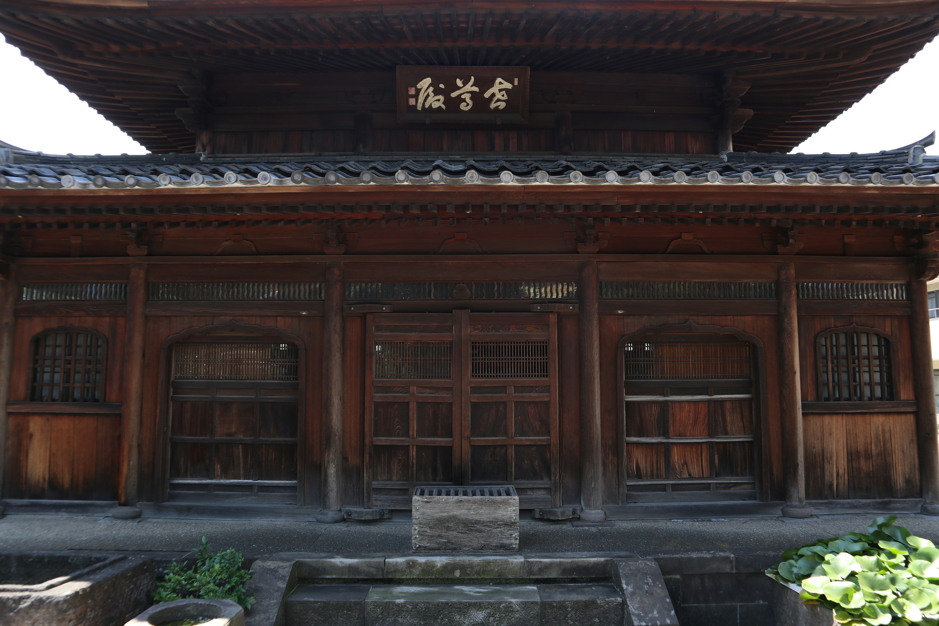 Front view of a traditional wooden building featuring windows and doors with an old-style roof and a sign in kanji