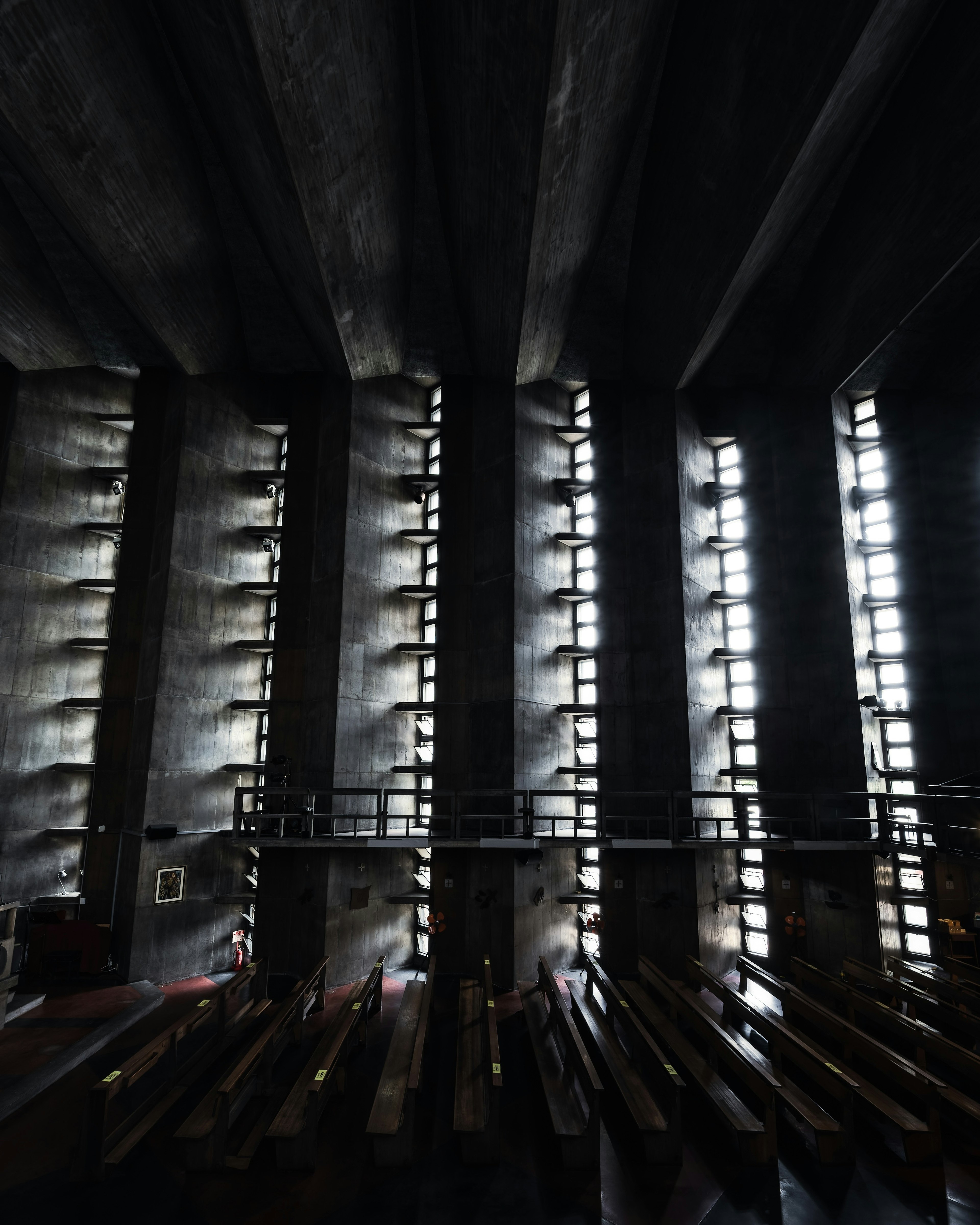 Interior de una iglesia oscura con tiras de luz a lo largo de las paredes y bancos de madera