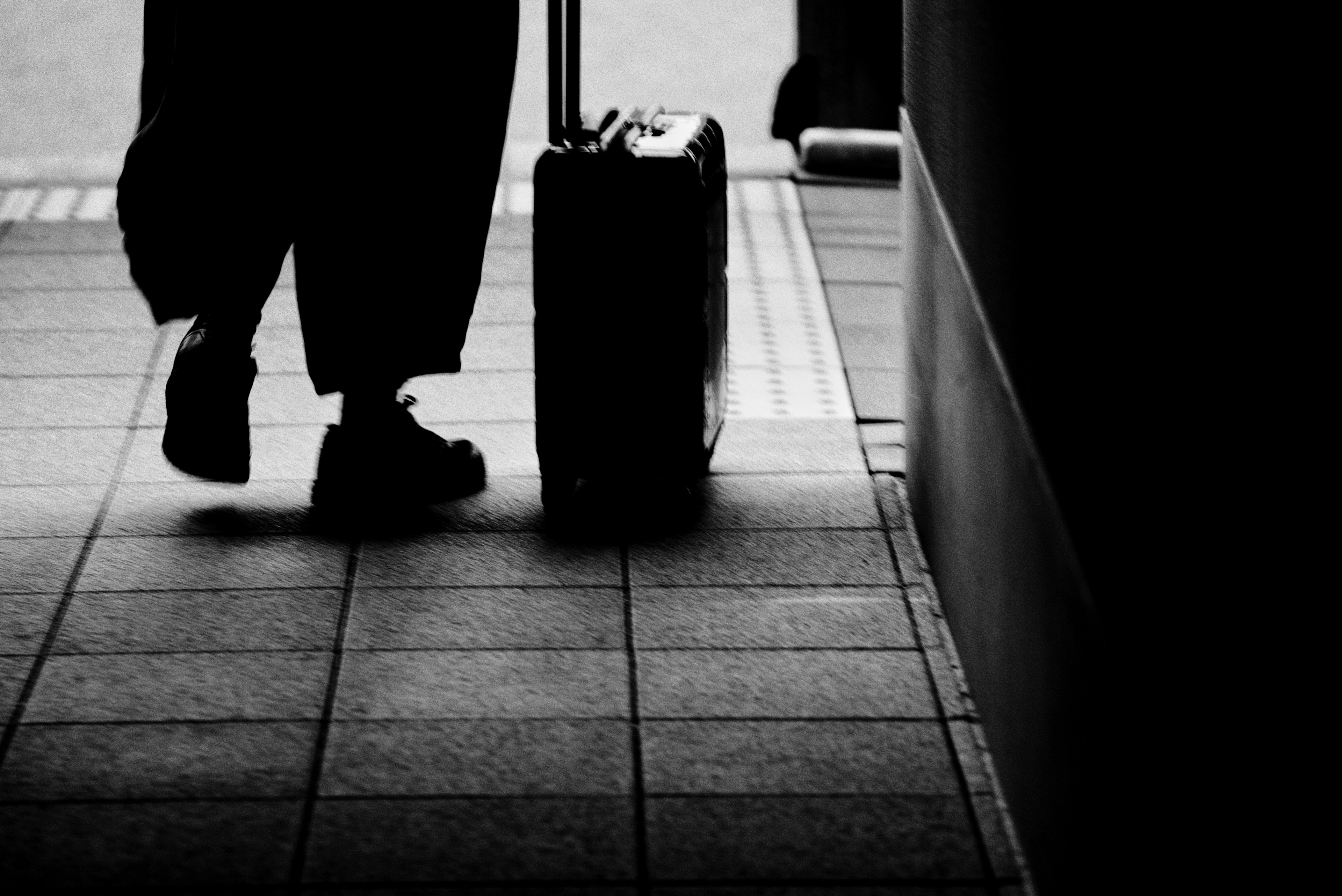 Silhouette of a person pulling a black suitcase in a corridor