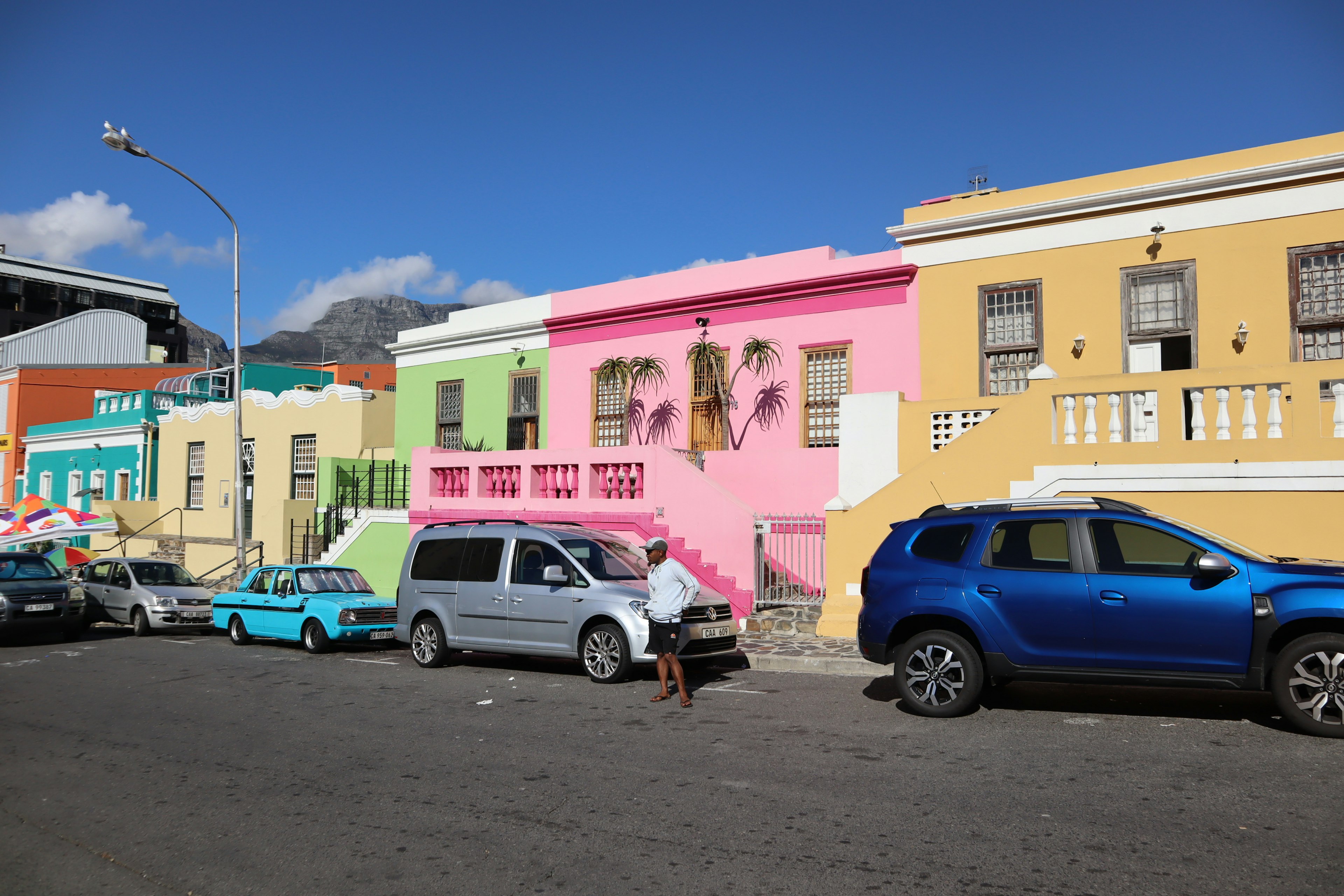 Colorful houses lining the street with parked cars and a person