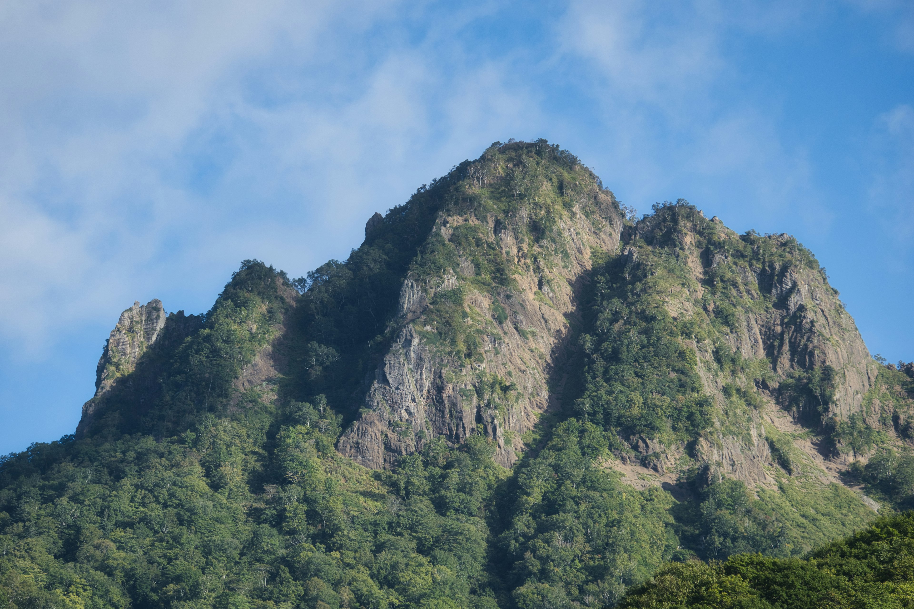 一座绿色覆盖的崎岖山峰在蓝天下耸立