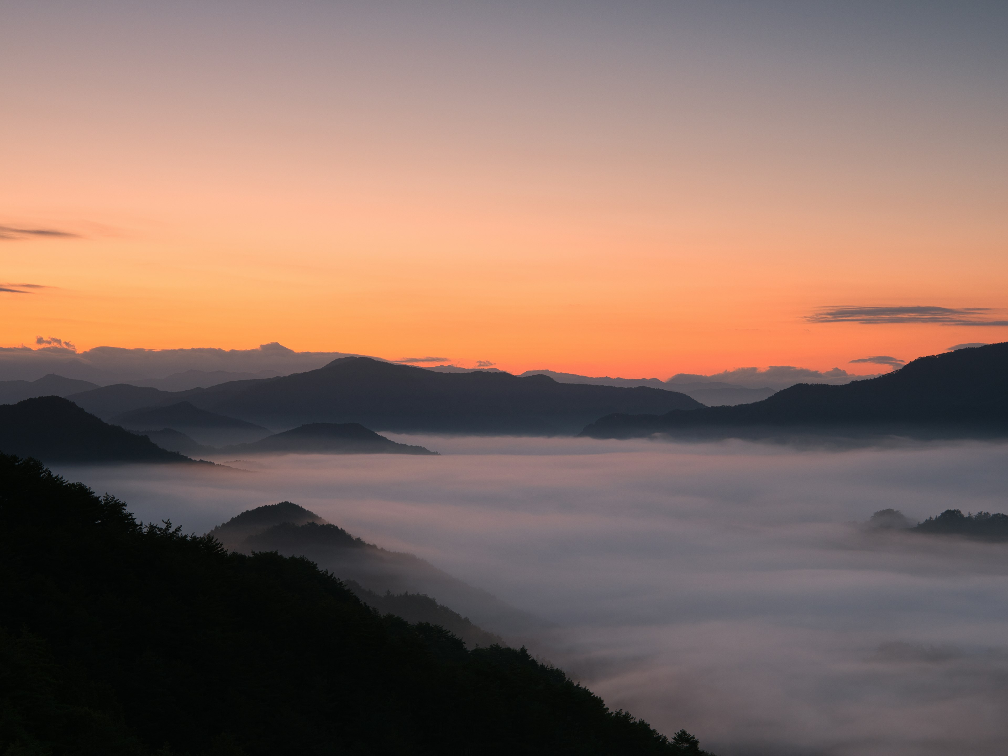 Schöne Landschaft von Bergen, die in Nebel gehüllt sind, mit einem Sonnenuntergangshimmel