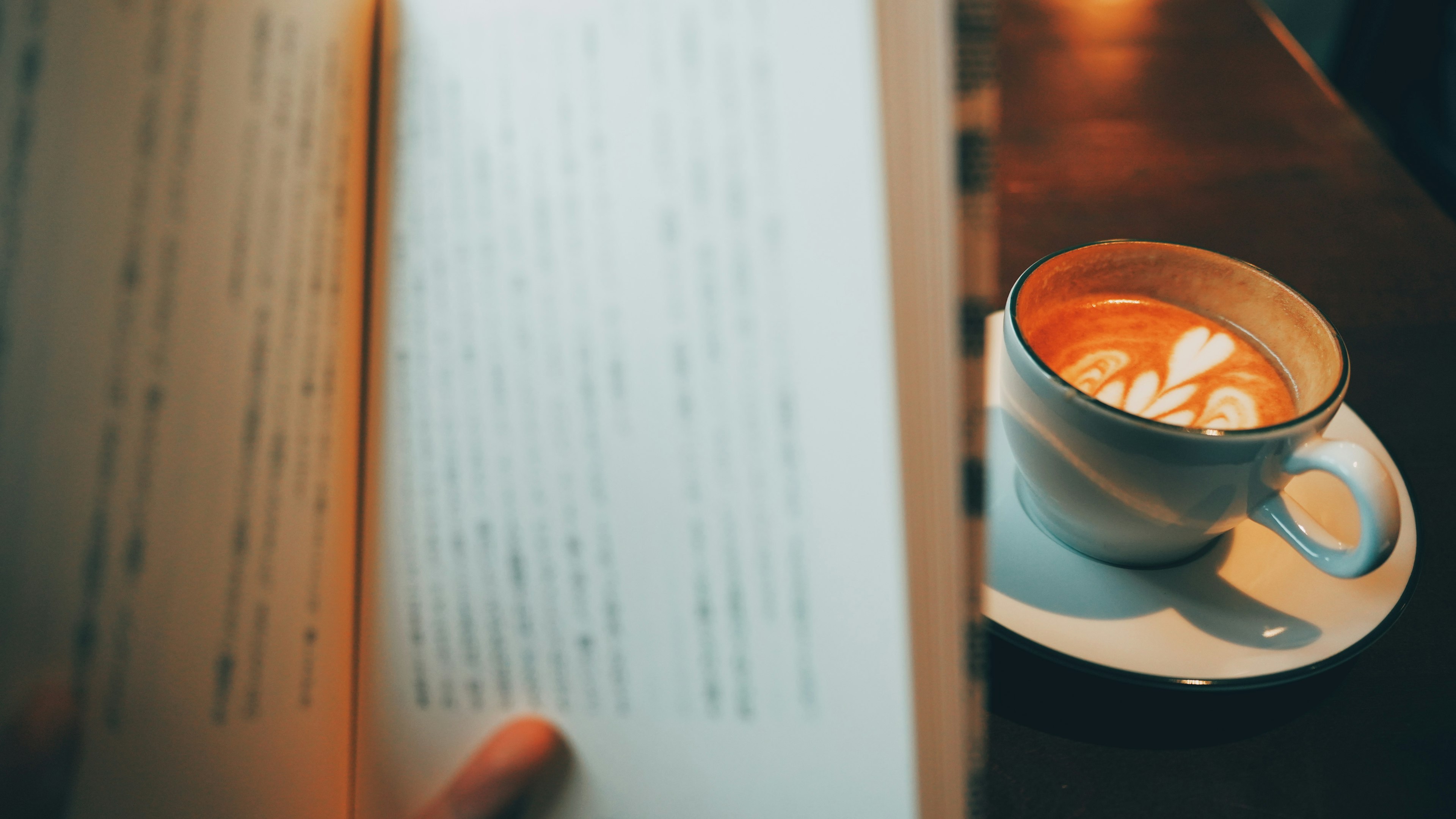 Une scène confortable avec une main tenant un livre et une tasse de café au premier plan